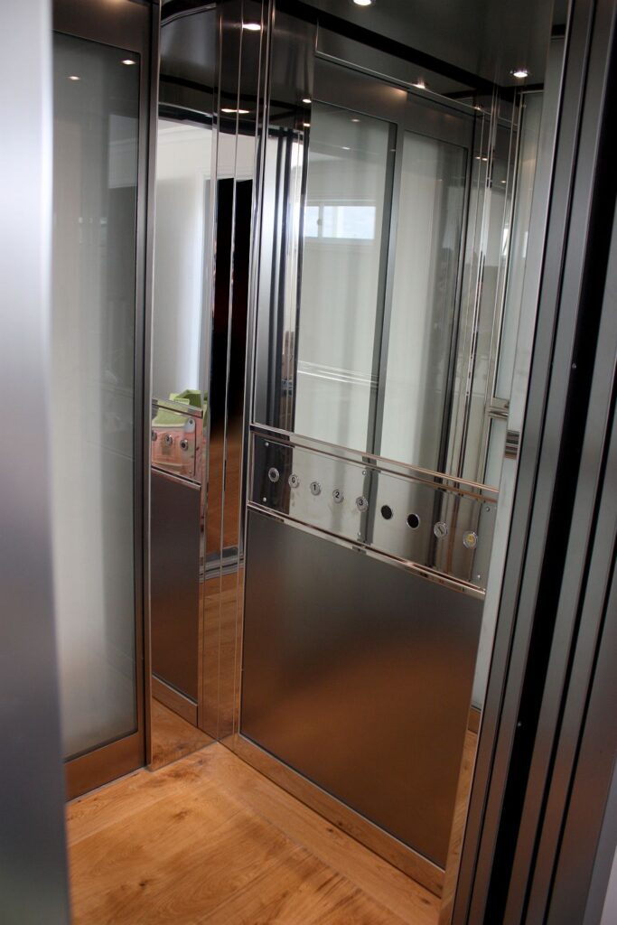 Inside the ElfoLift 2 cabin: brushed stainless steel skinplate, half-height mirror and a glass panel over a timber floor