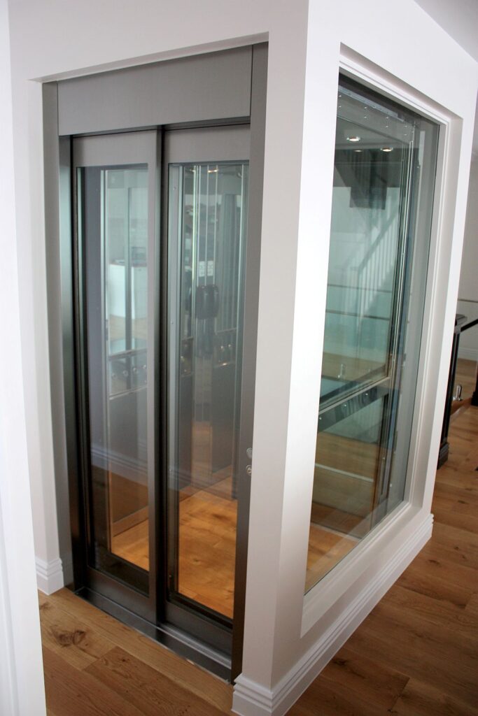 Glass-fronted ElfoLift 2 landing door set into a white shaft surround, with a glass side panel, in a Queenslander-style home