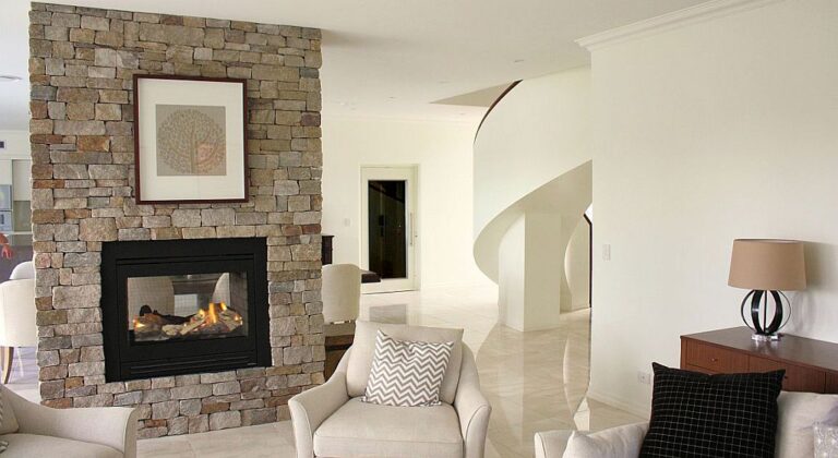 Living area with a stone fireplace feature wall, the curved staircase and the white lift door in the Indooroopilly home