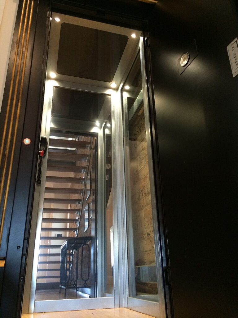 Inside the black lift car at Manly Cove, with downlights, mirrored walls and a glass wall facing the timber staircase