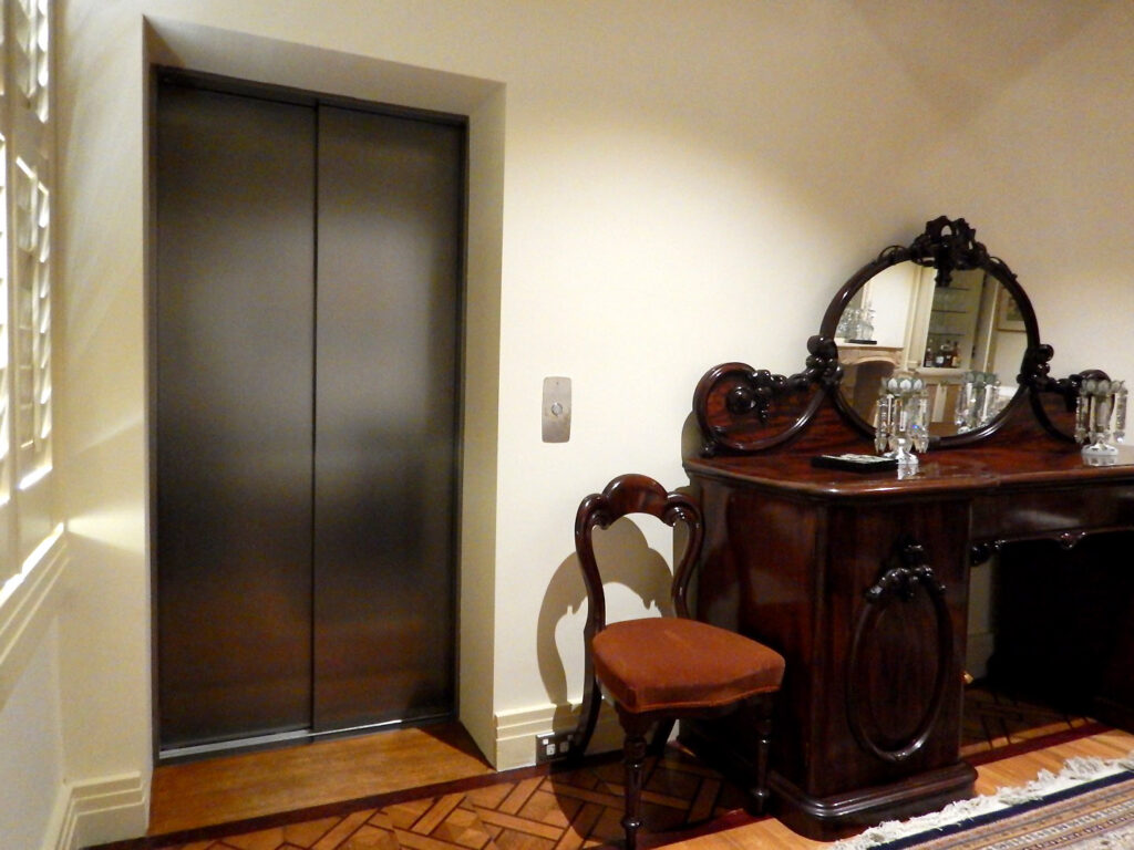 Closed lift doors with a brushed finish beside an antique sideboard in a Melbourne home