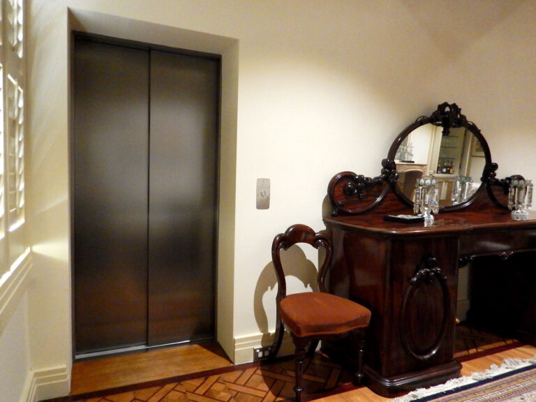 Closed lift doors with a brushed finish beside an antique sideboard in a Melbourne home