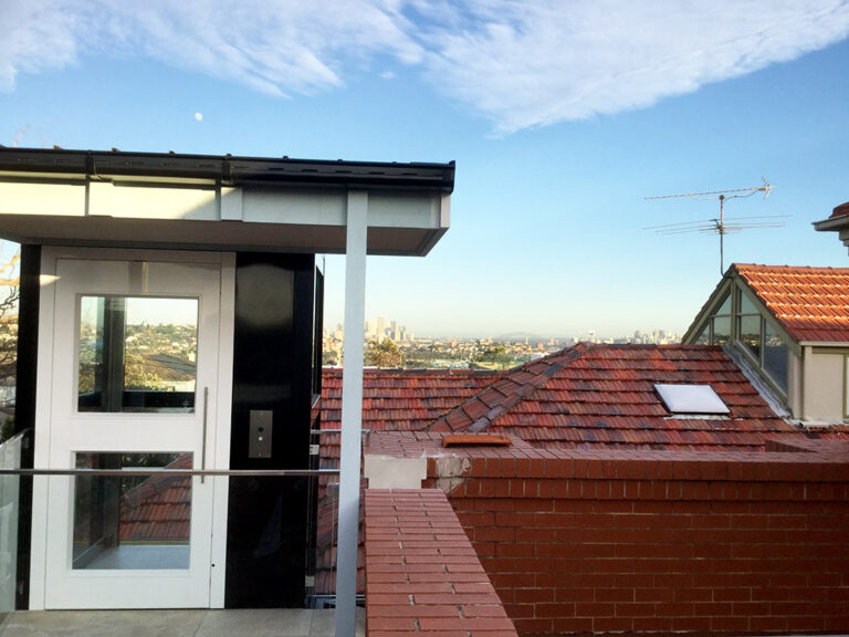 White lift door at roof level beside red tile roofs and a skyline in Dover Heights