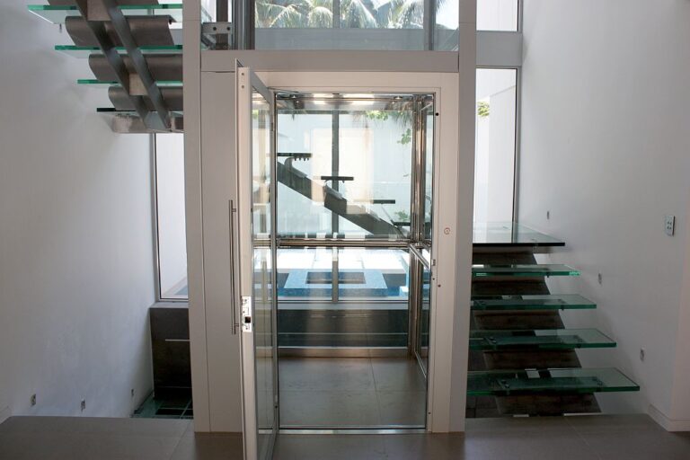 Glass lift seen through the stairwell with glass stair treads and a palm outside