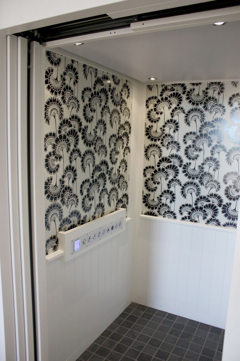 Lift cabin interior with black and white floral wallpaper, white panelling and a tiled floor