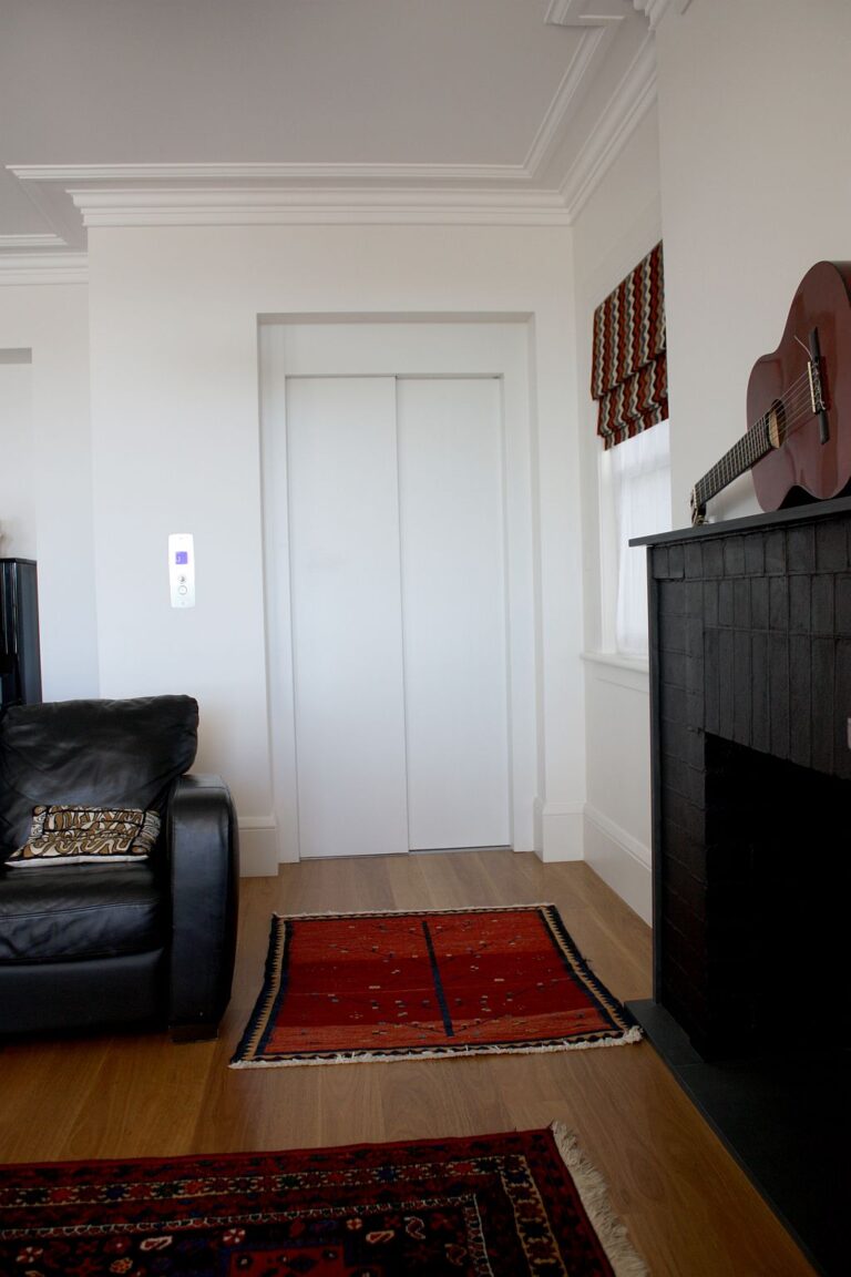 Closed lift door in a living room beside a black fireplace and black leather sofa