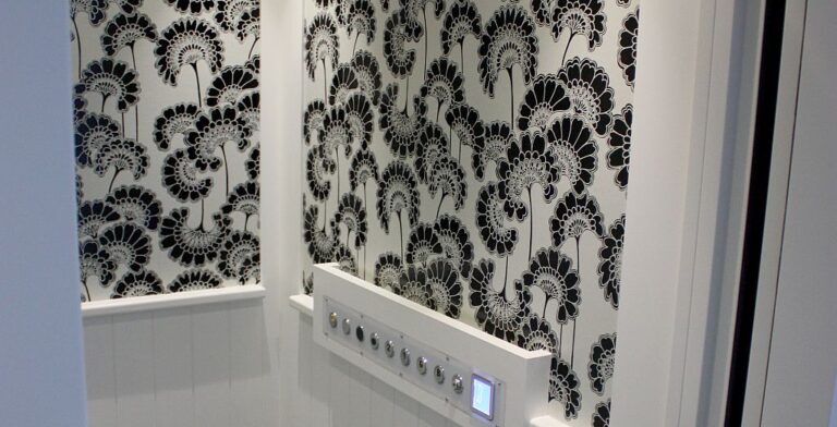 Lift cabin wall with black and white floral wallpaper and a row of push buttons