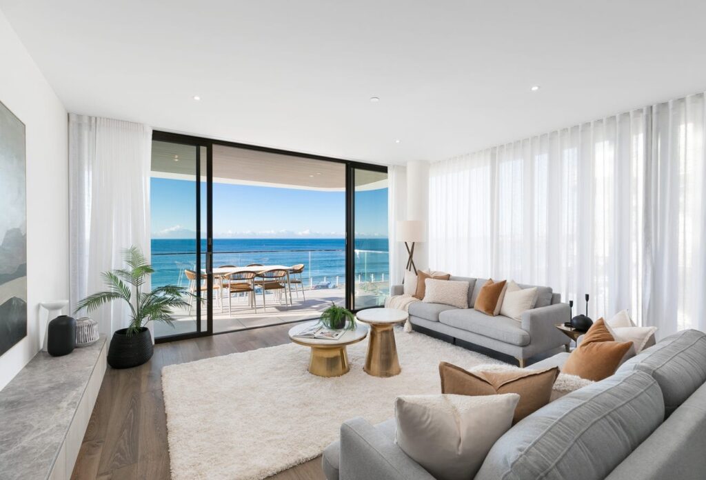 Living room with a grey sofa and sliding glass doors opening to a balcony and ocean view at Solstice, Cronulla