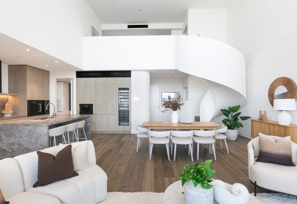 Open-plan Solstice apartment with a kitchen, dining table and a white spiral staircase rising to the upper level