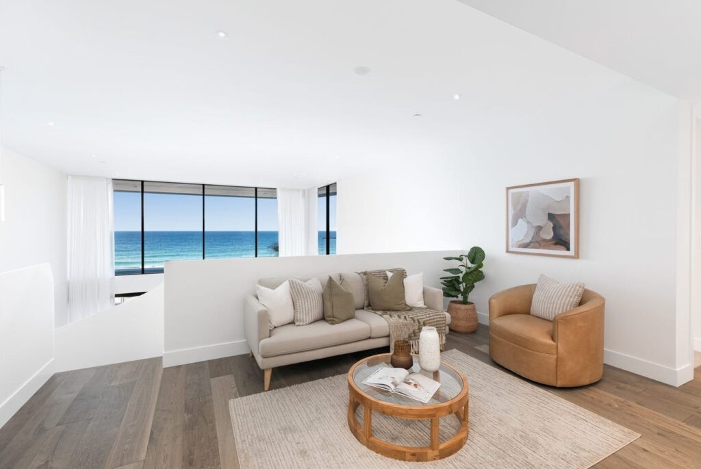 Light-filled upper living area at Solstice with a sofa, tan armchair and ocean views through the windows