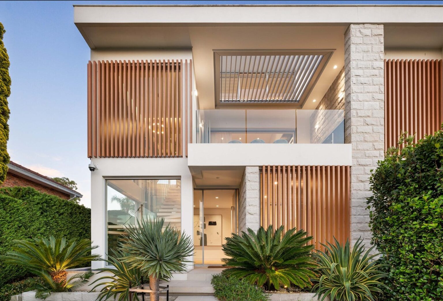 Front of the Gladesville home at dusk, with timber battens, a stone feature wall and landscaped garden