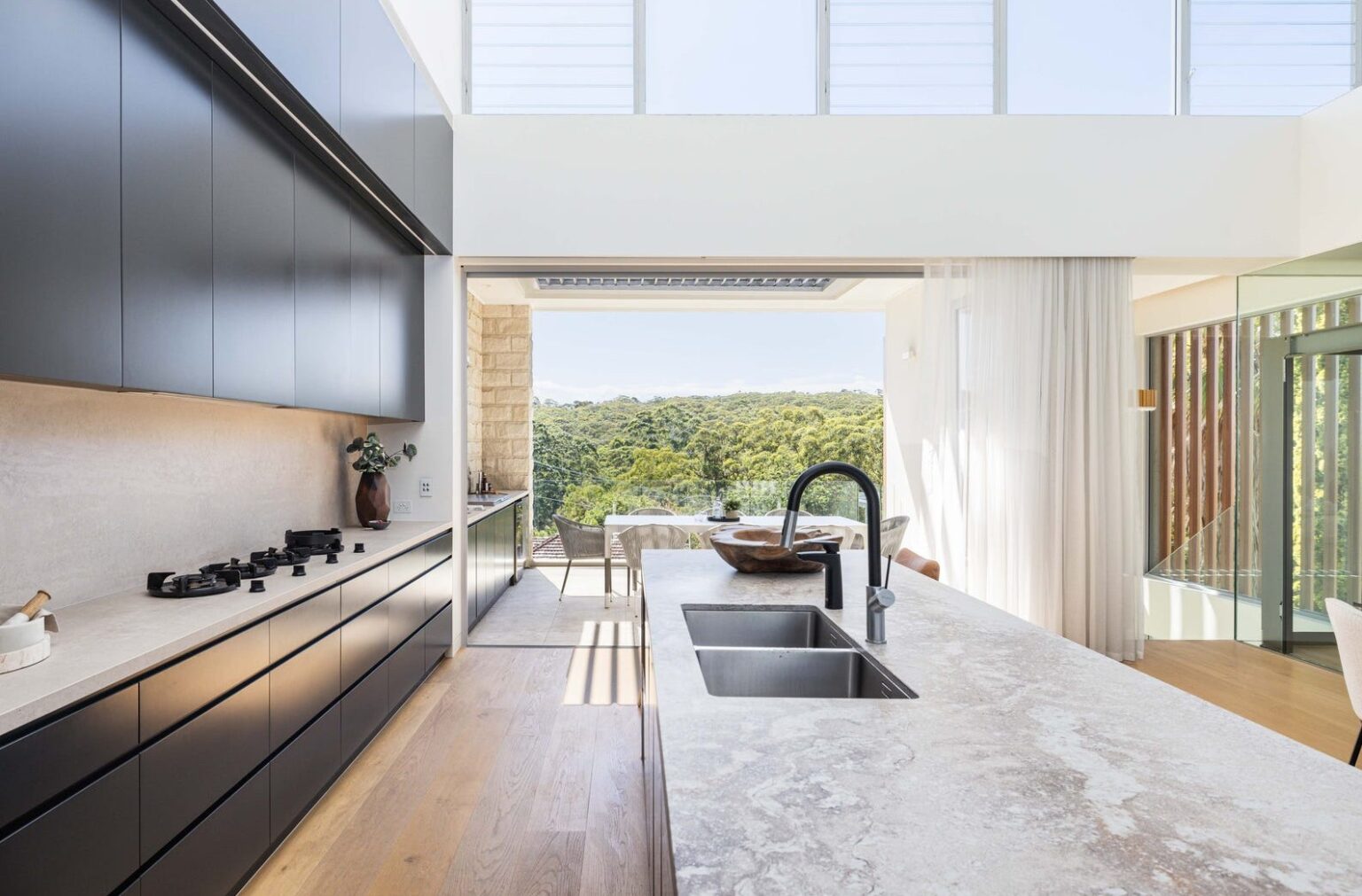 Kitchen opening to the terrace and treetop view, beside the glass lift shaft in the Gladesville home