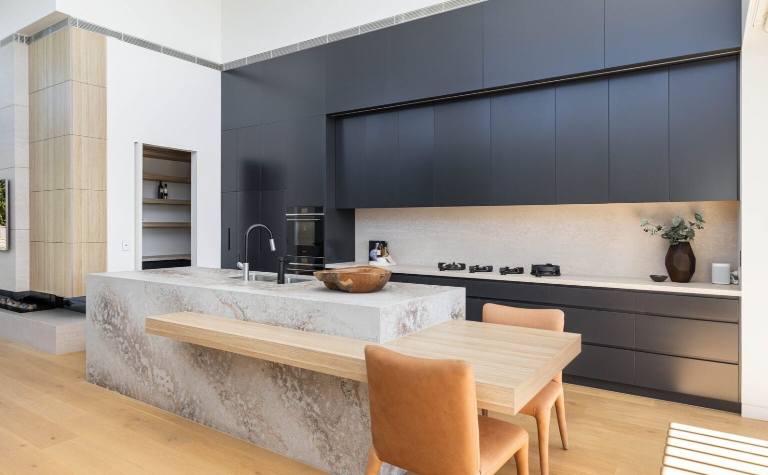 Open-plan kitchen with dark cabinetry, a stone island and a timber dining bench in the Gladesville home