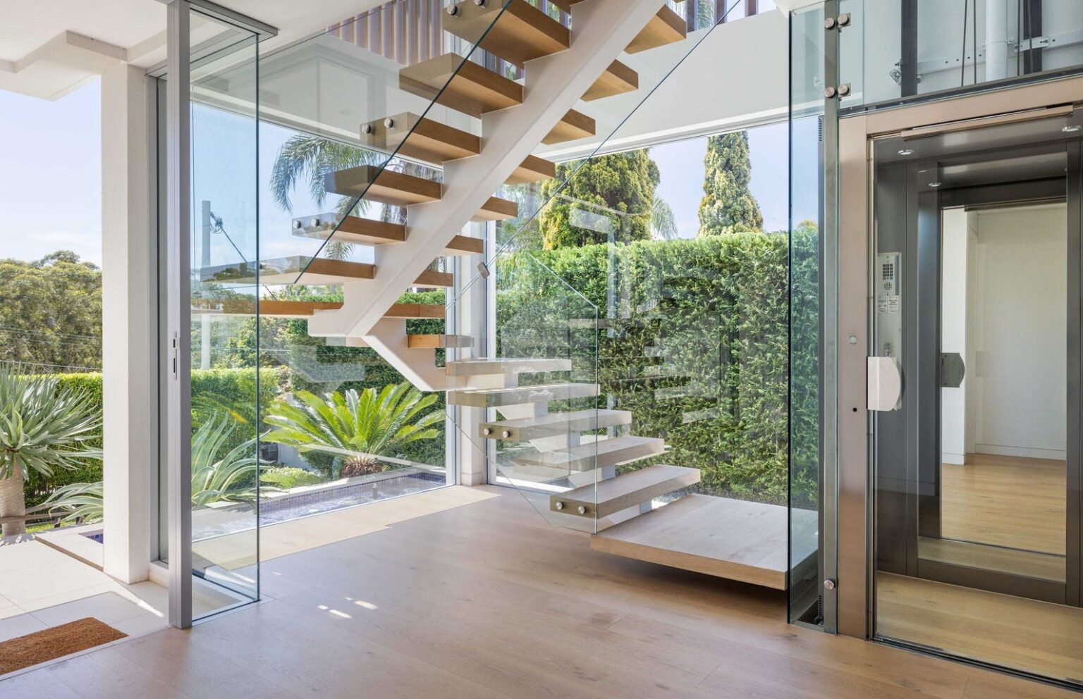 Floating timber staircase beside the frameless glass shaft and A Series glass lift in the Gladesville home