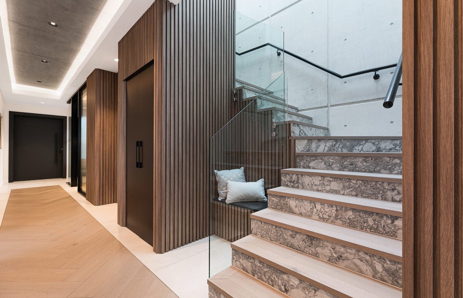 Luxury home lift positioned beside timber staircase with stone treads and glass balustrade in Caringbah South