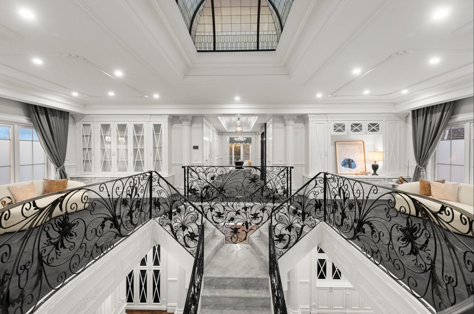 Looking down the double-height void past wrought-iron balustrades to the marble stair in a Balwyn home