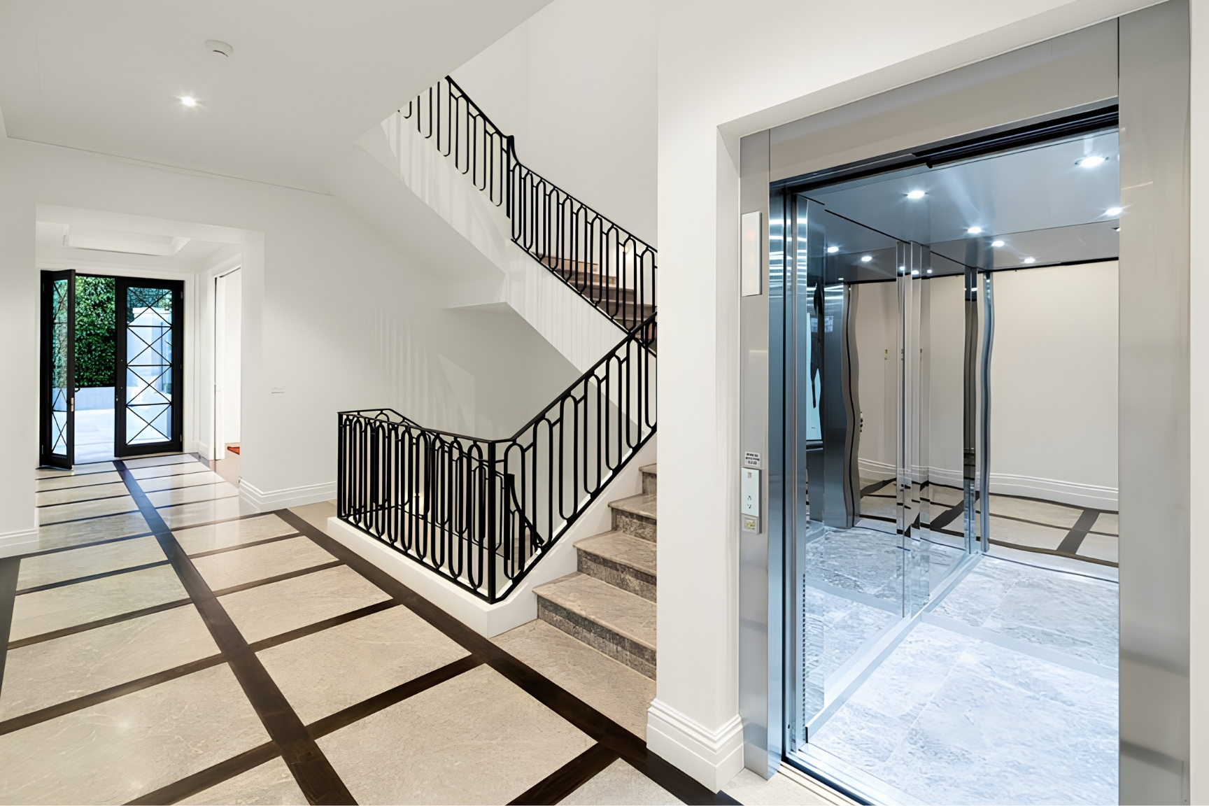 Lift Shop home lift with mirrored cabin walls, stainless steel frame and custom stone flooring beside a staircase