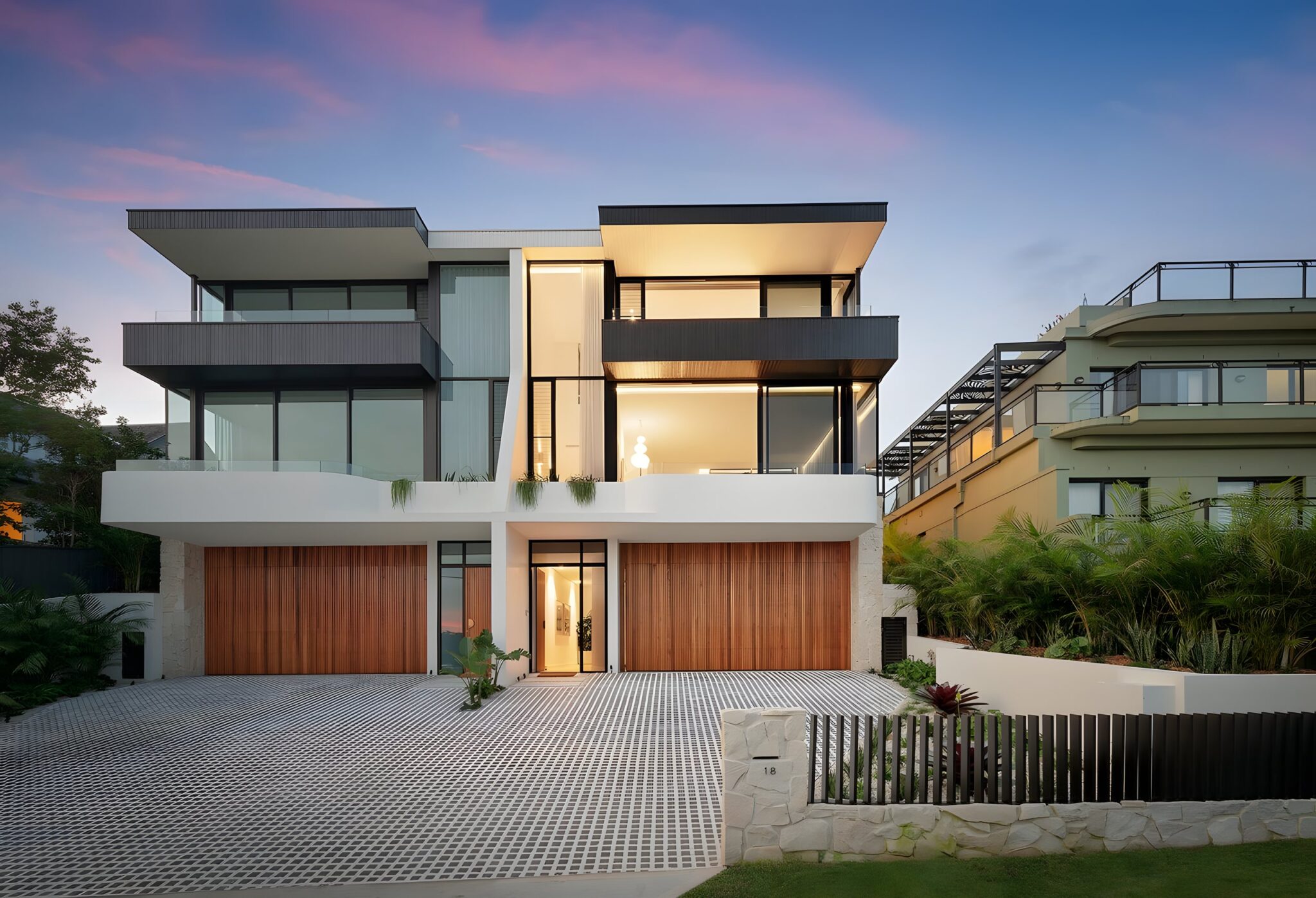 Three-level Fairlight home at dusk with a concrete and glass facade and timber garage doors