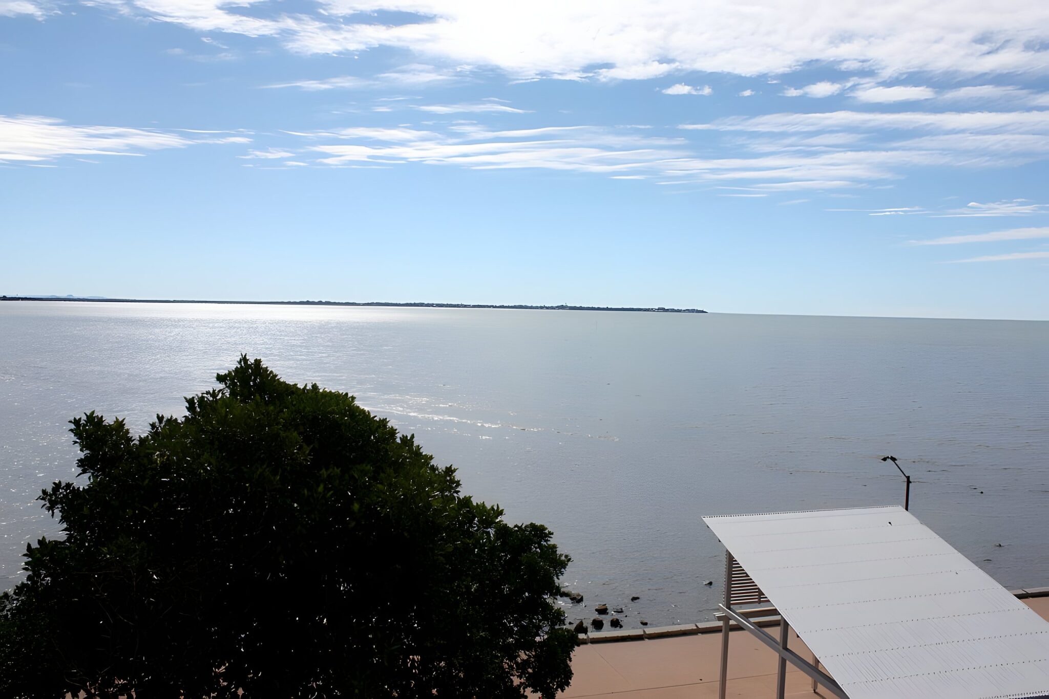 Bay water view from a home in Shorncliffe, with a tree in the foreground and a jetty roof at the edge of the frame