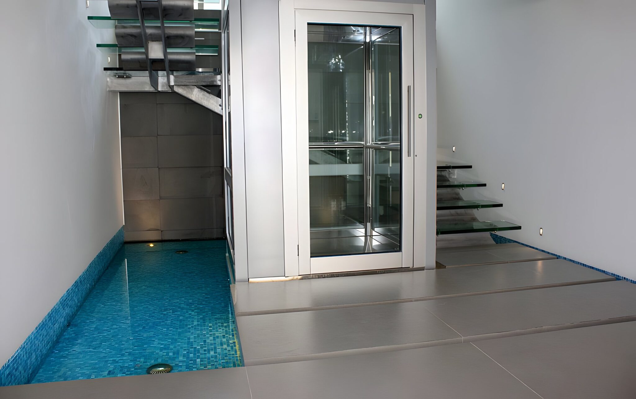 Glass lift door beside a blue mosaic pool with floating stepping tiles at the entry of a City Beach home in Perth
