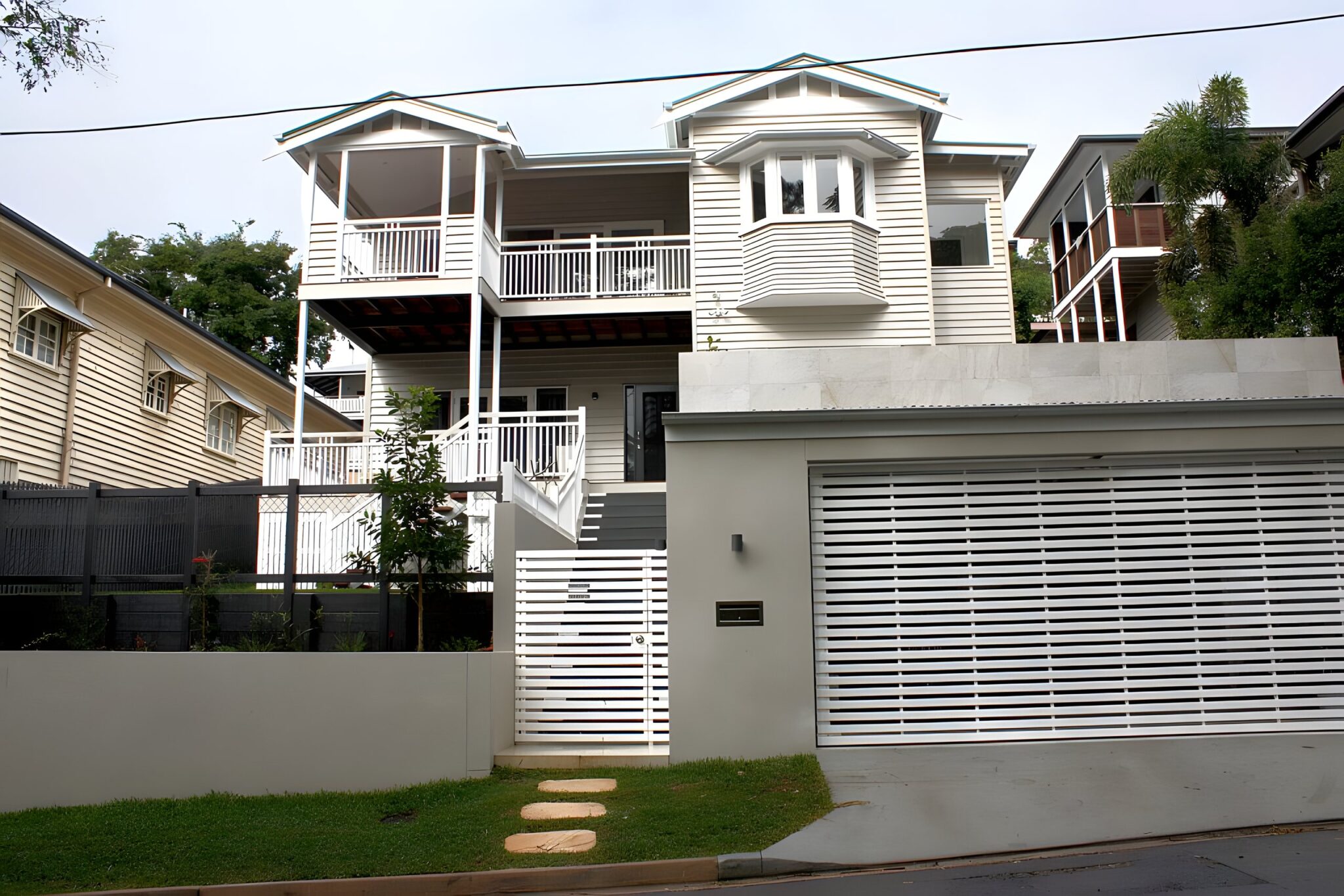 Two storey Queenslander style home with white timber balustrades and a slatted garage door in Brisbane