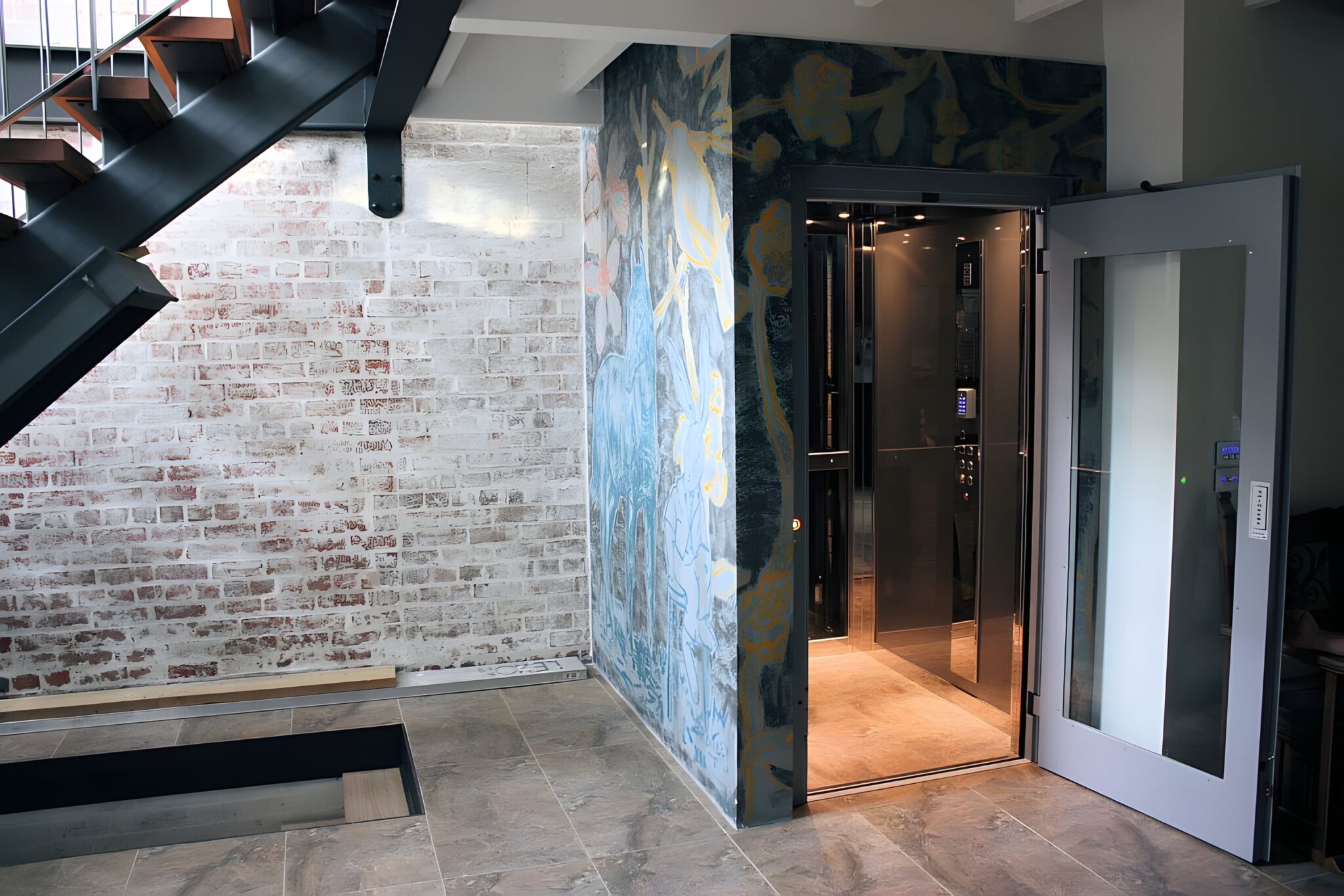 Open E1 lift door beside an exposed brick wall and hand-painted shaft artwork in the converted Collingwood factory