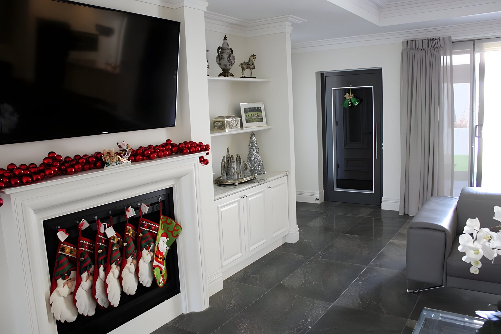Living room in the Coogee home with a fireplace hung with stockings and the dark grey lift door beyond