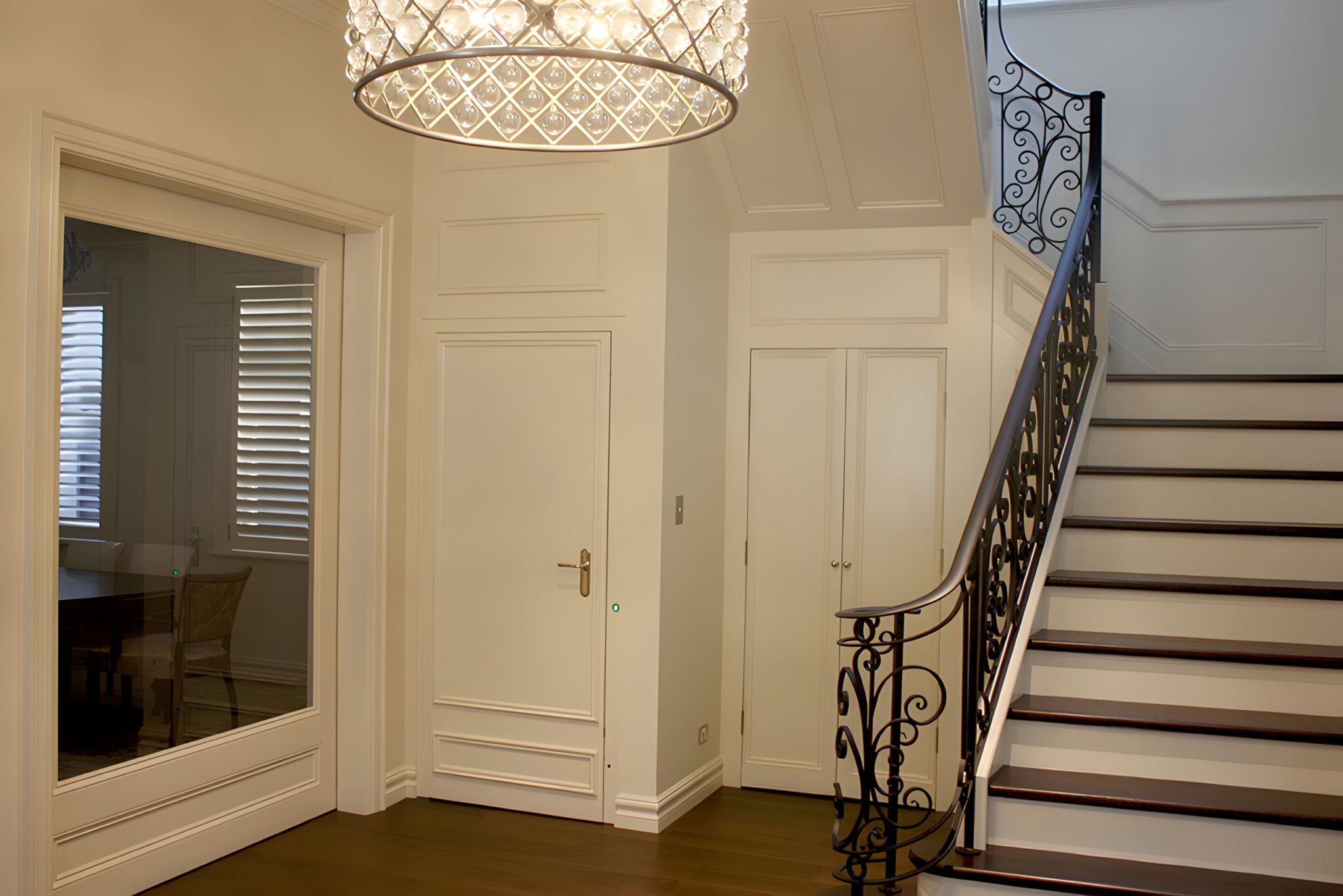 Entry hall in Tamarama with a crystal chandelier, wrought iron stair rail and white panelled walls