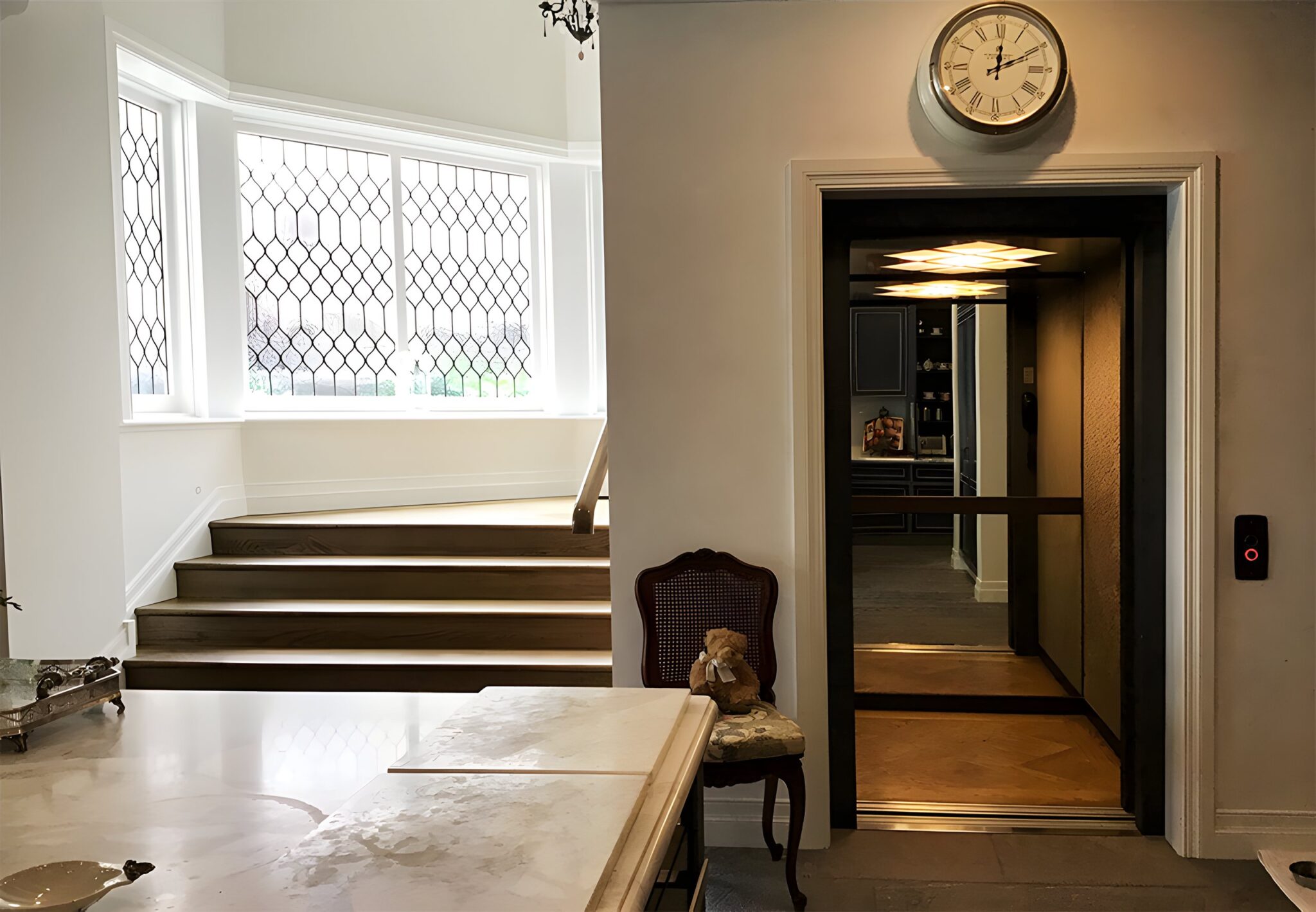 Hallway lift doorway with a dark door beside timber steps and a leadlight bay window in a Sydney home