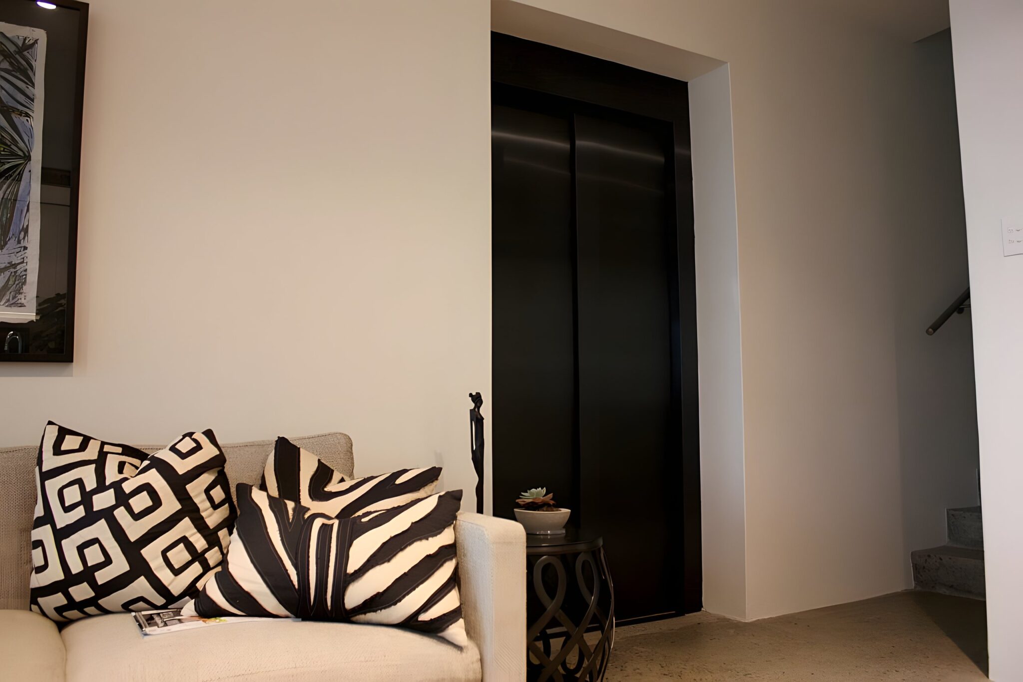 Closed dark Inox Nero Satinato lift doors in the wall above a sofa with patterned cushions