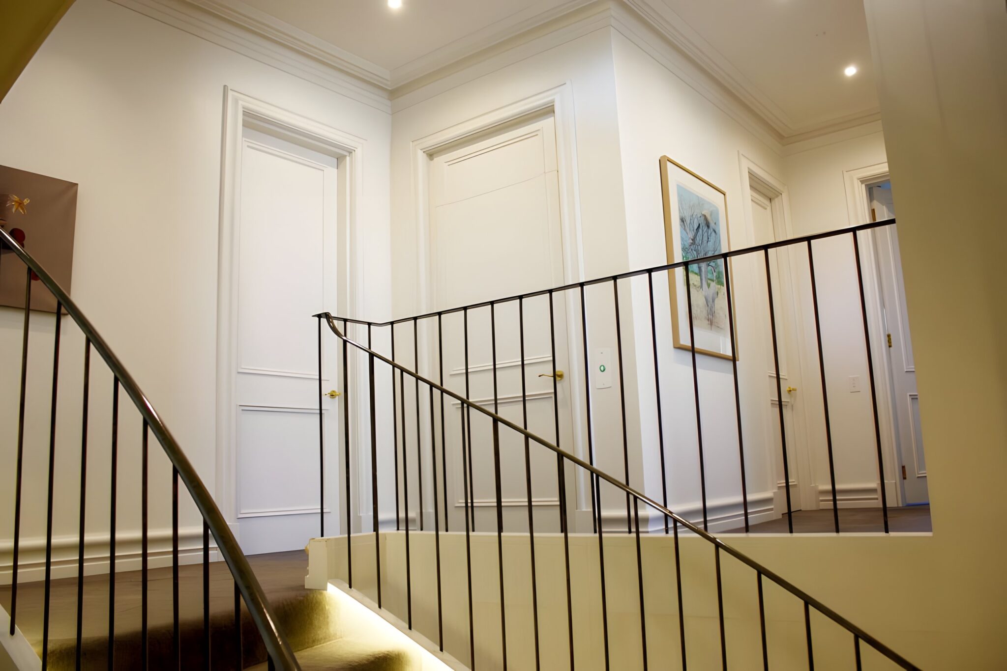 Landing of a Sydney Harbour beachfront home with a black balustrade, white panelled doors and a framed artwork