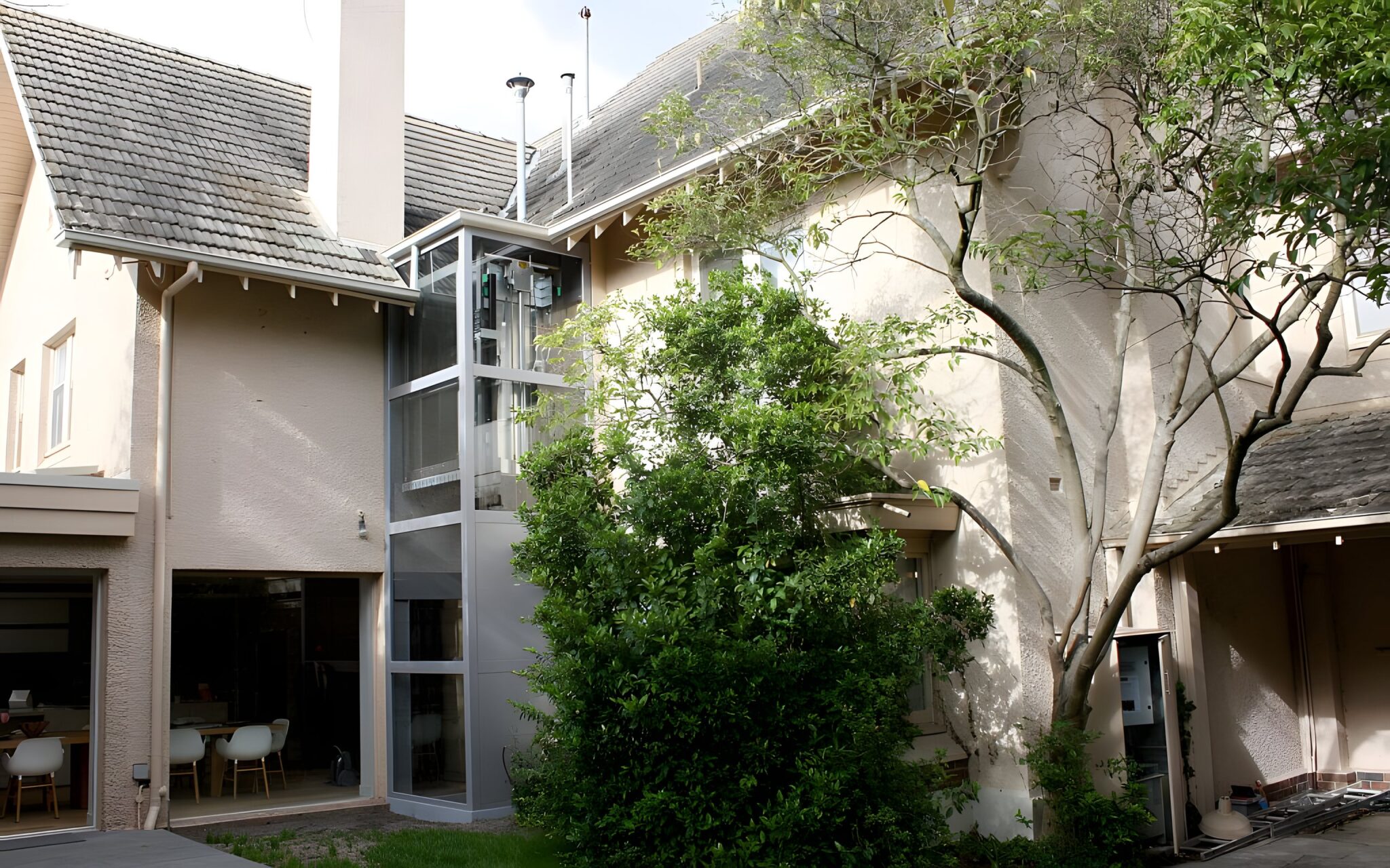 External glass lift shaft on the rear of a Sydney house, tucked beside a tree in the garden