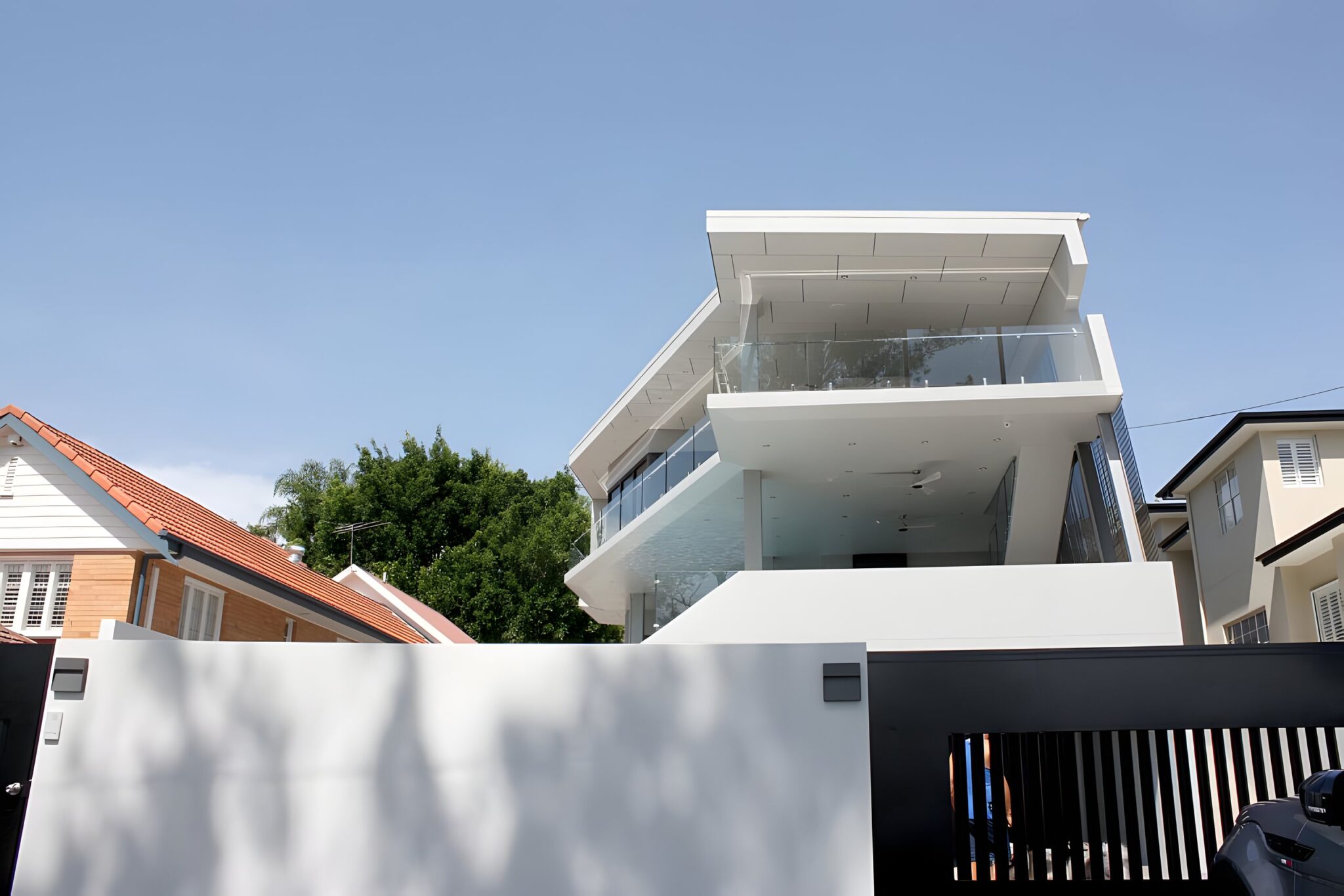 Three-storey white builder's own home with glass balconies behind a high white wall near Brisbane