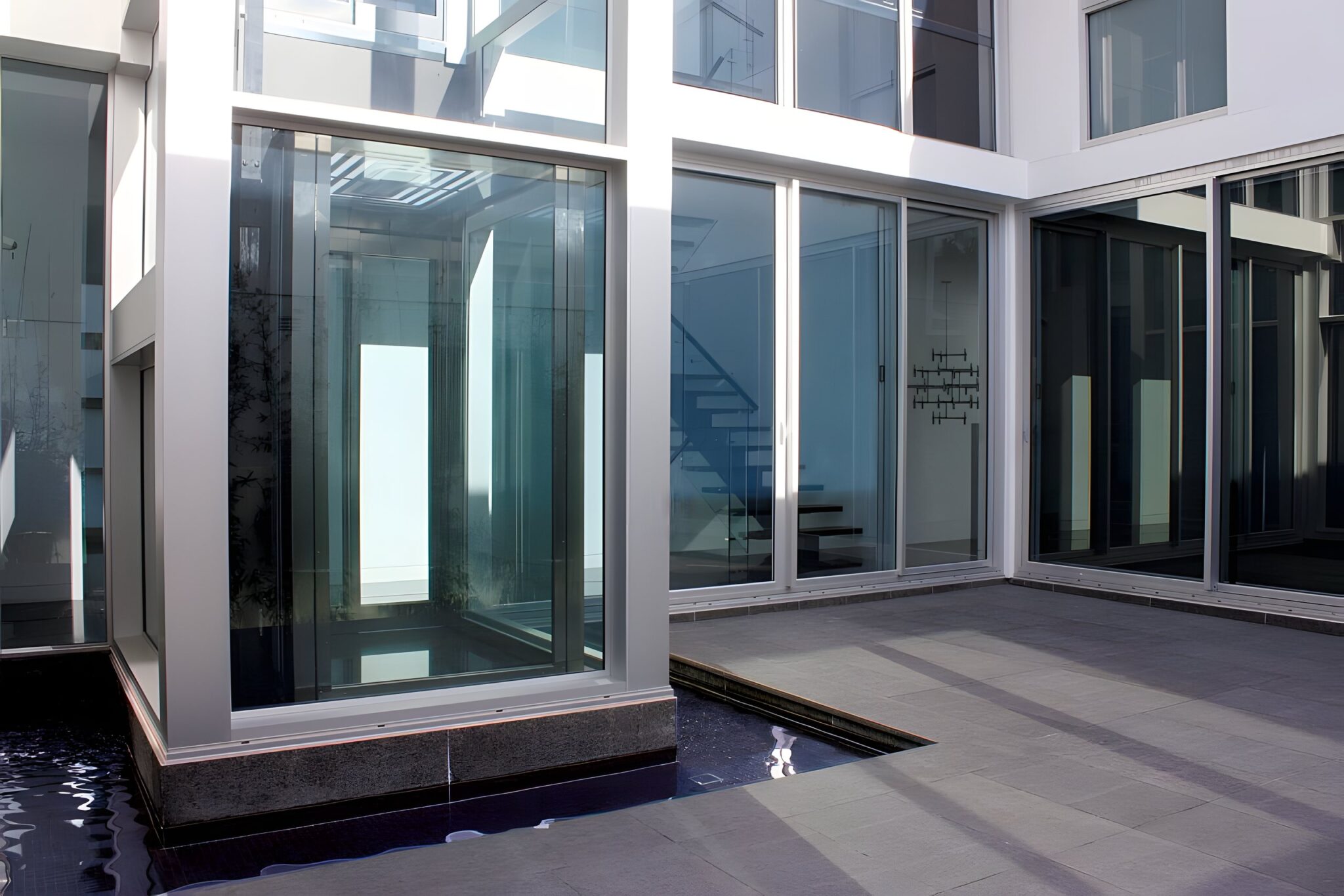 Glass lift shaft forming the corner of a Dover Heights home, beside the courtyard pond