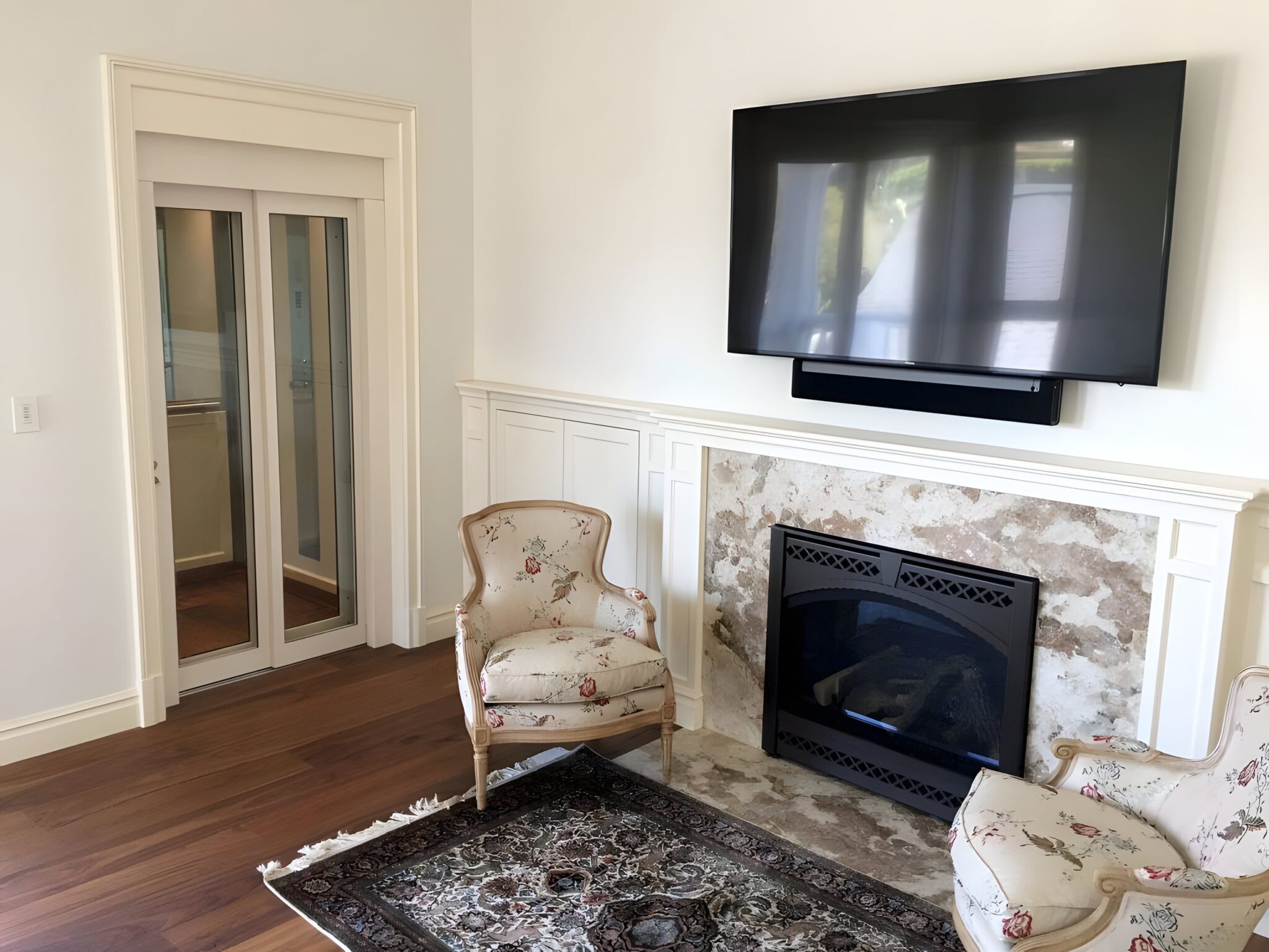 Cream glass-panelled lift door in a white architrave beside a marble fireplace in a Westwood home extension