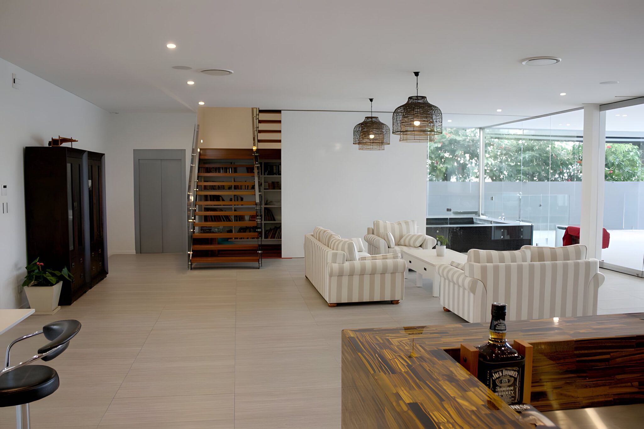 Open plan living area of a new Sydney estate home with a timber staircase, striped sofas and the lift door beside the stairs