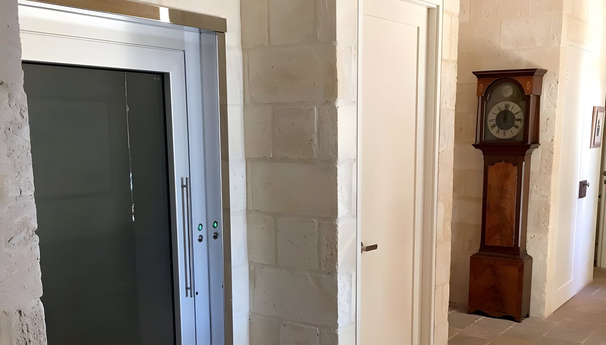 Lift door with an aluminium frame beside a limestone wall and a grandfather clock in a Cottesloe home
