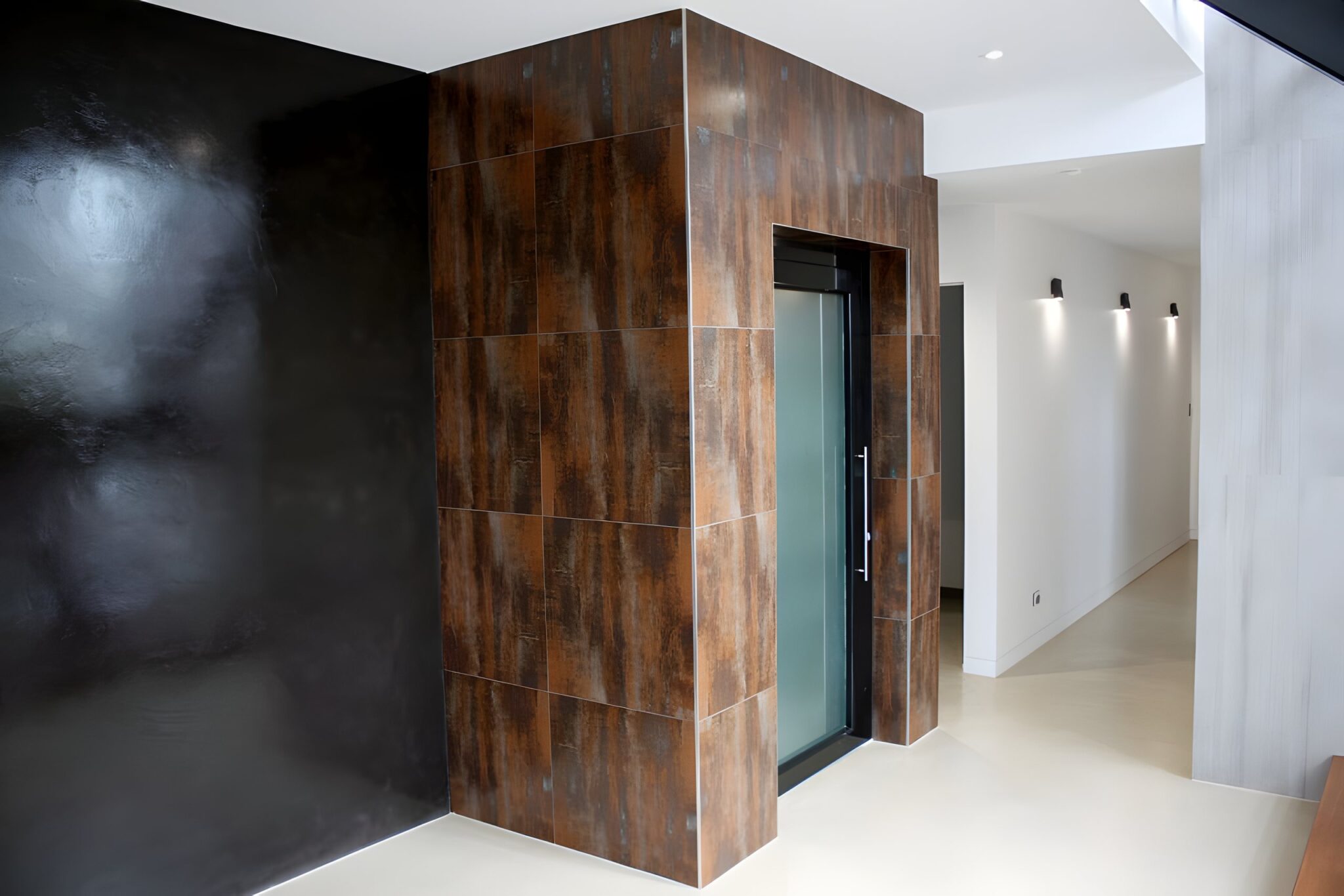 Rust-coloured tile feature wall enclosing a lift with a frosted glass door beside a black wall in a Newmarket home