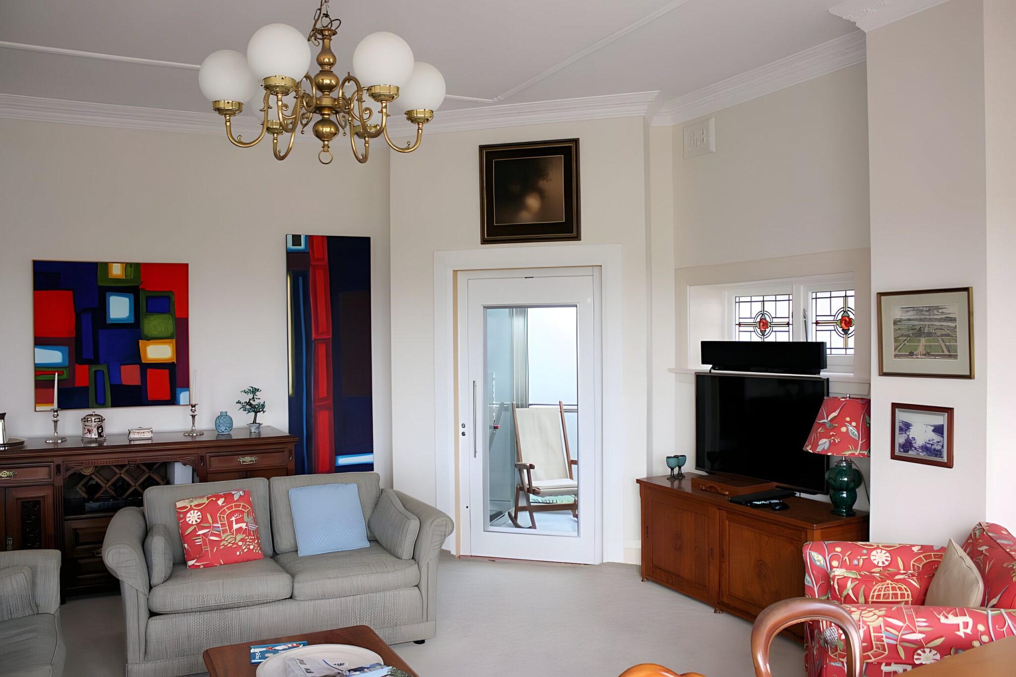 Period living room in Mosman with a chandelier, and a white lift door with a glass panel set in the wall beside the television