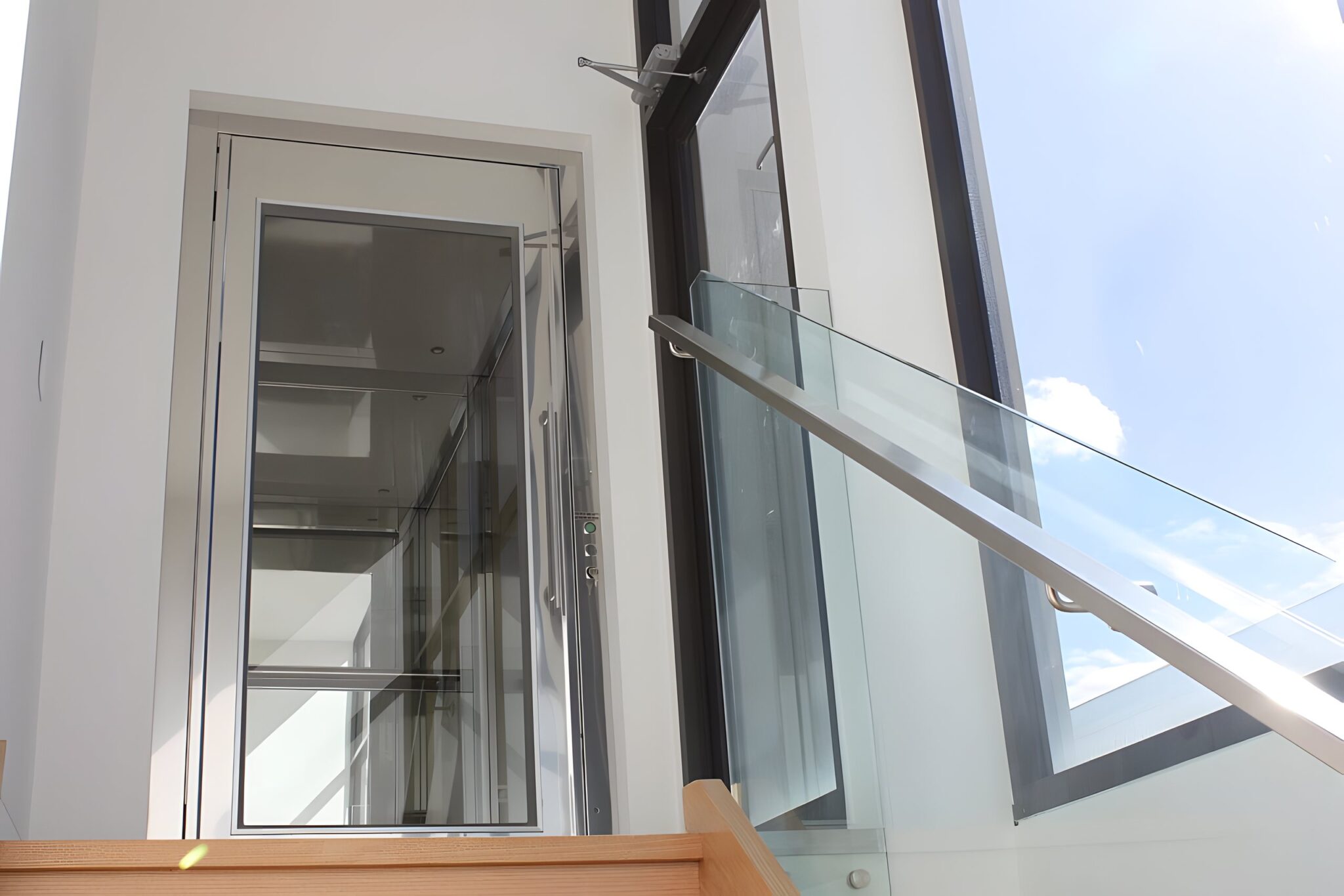 Glass-panelled home lift door at a landing beside a glass balustrade and tall windows in a Port Melbourne home