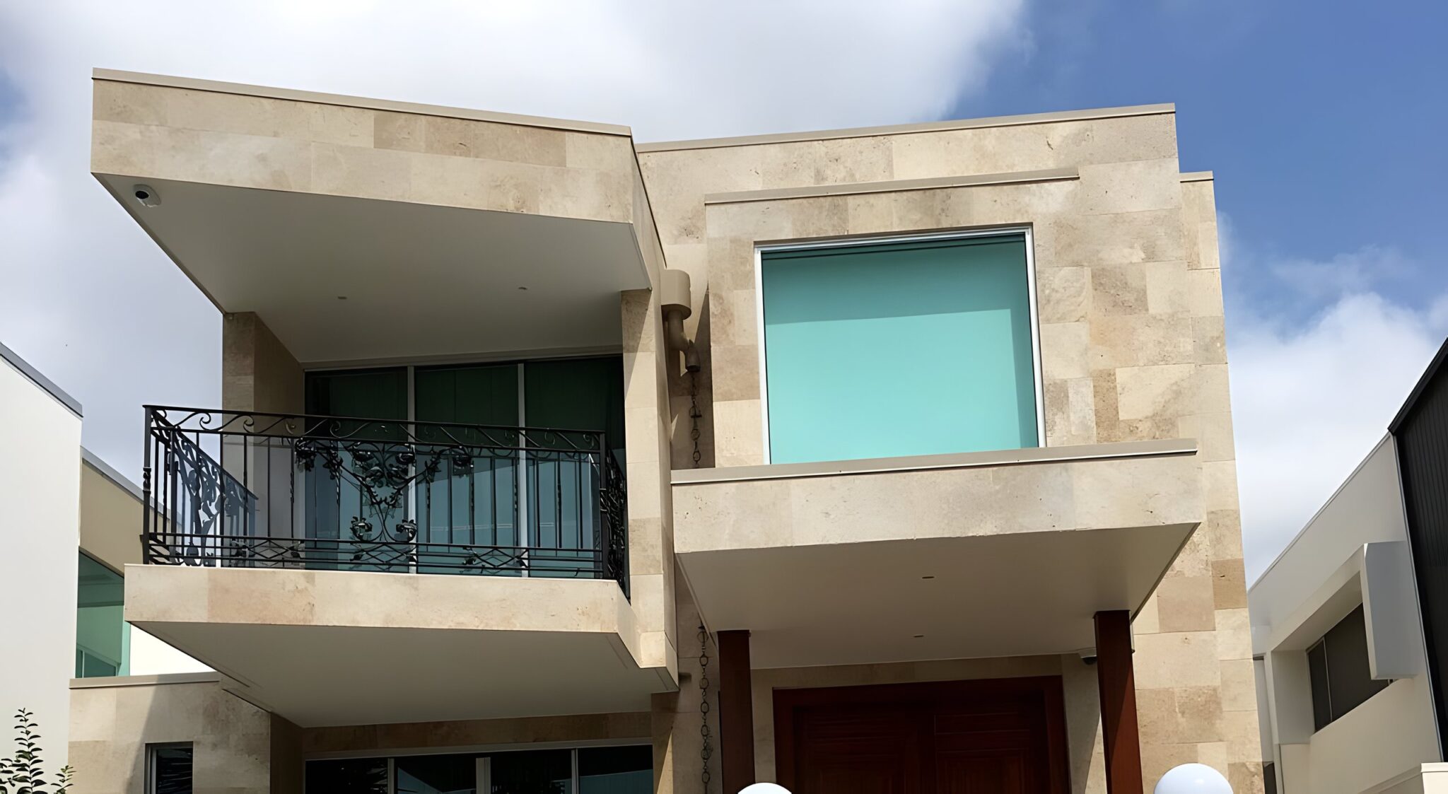 Front of a stone clad four-level riverfront home in Bulimba with a wrought iron balcony and teal glass windows