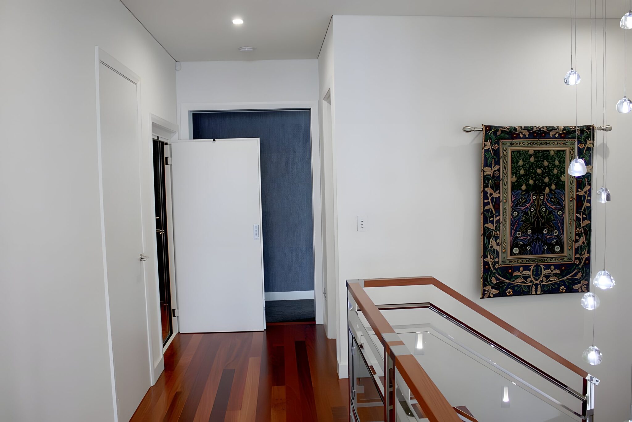 Upper landing of a Mount Pleasant home in Perth with a solid, near-concealed lift door beside gloss timber flooring and a glass balustrade