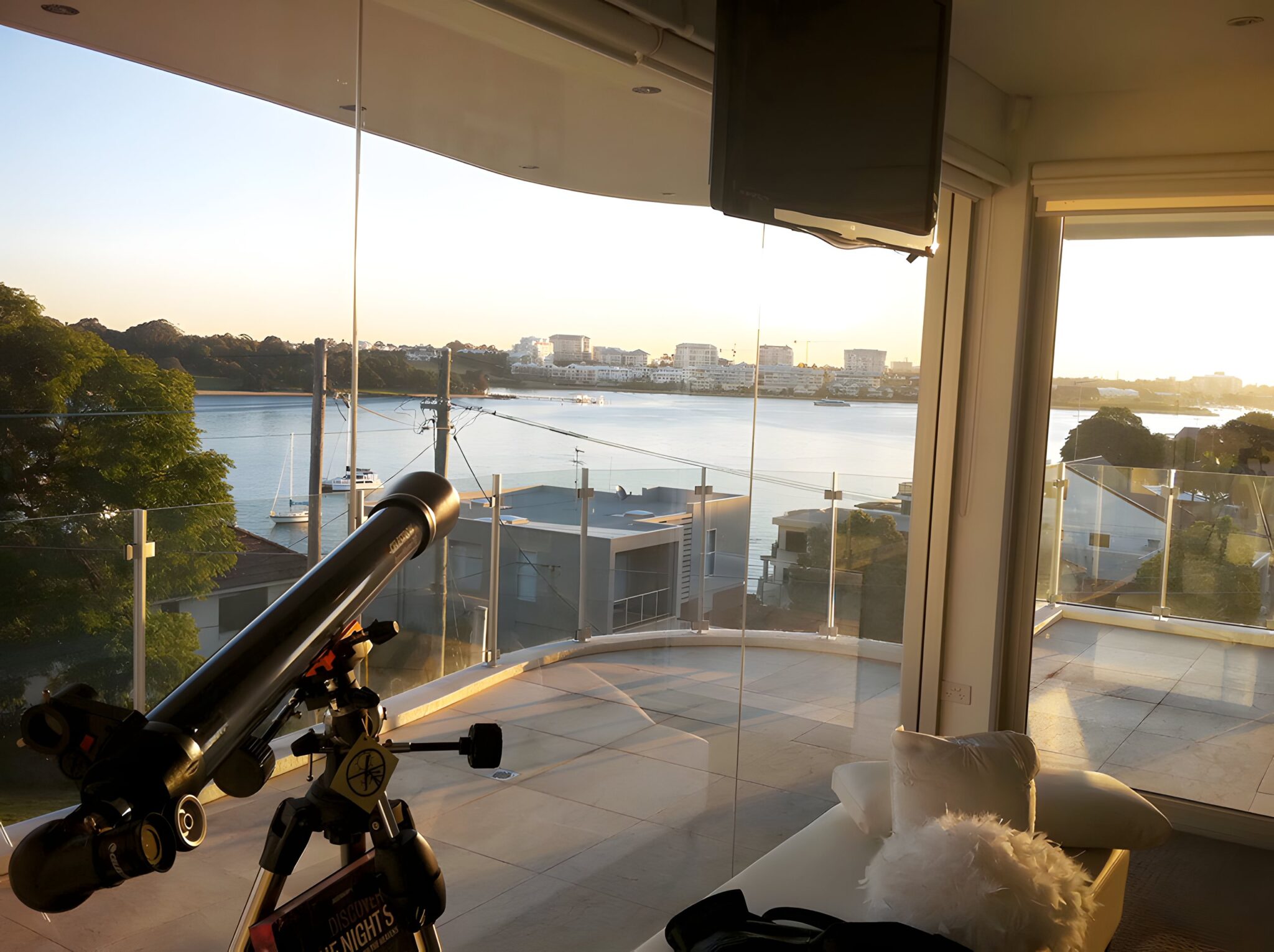 River view through the curved glass of the Parramatta River home, with a telescope on a stand