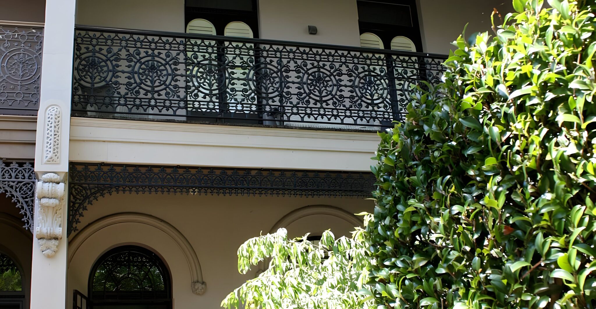 Ornate cast iron balcony balustrade on a terrace home beside a leafy tree in Glebe