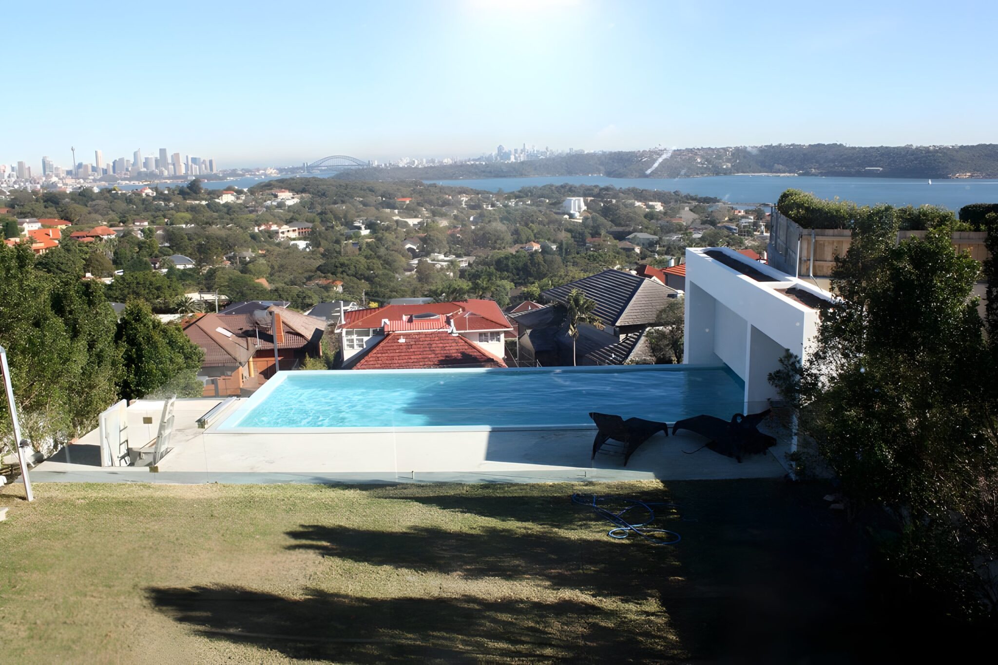 Sydney Harbour and the city skyline with the Harbour Bridge, seen over a hillside garden and swimming pool from an Eastern Suburbs home