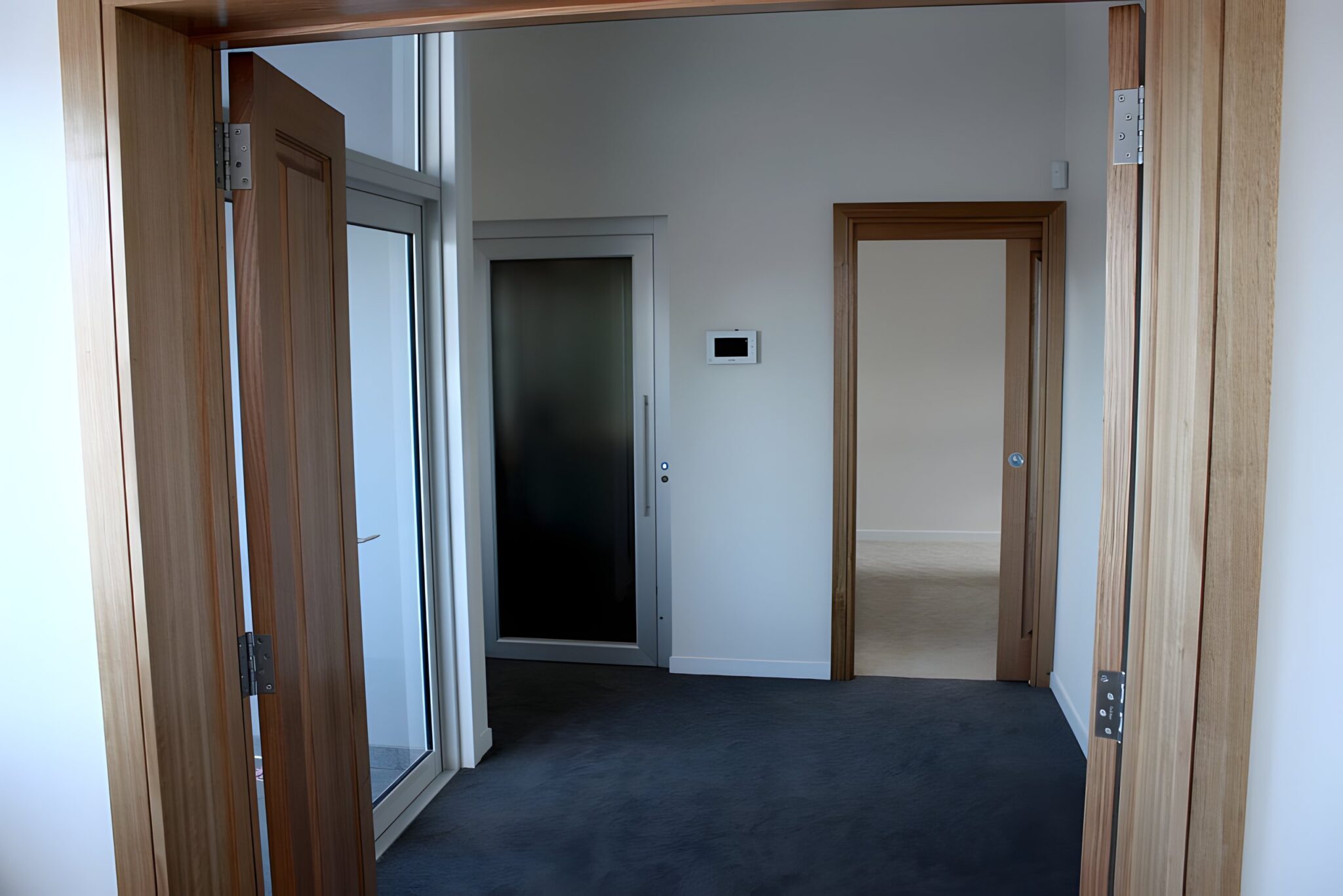 Timber framed doorway looking along a carpeted hallway to the lift door in the new extension of a heritage-style home