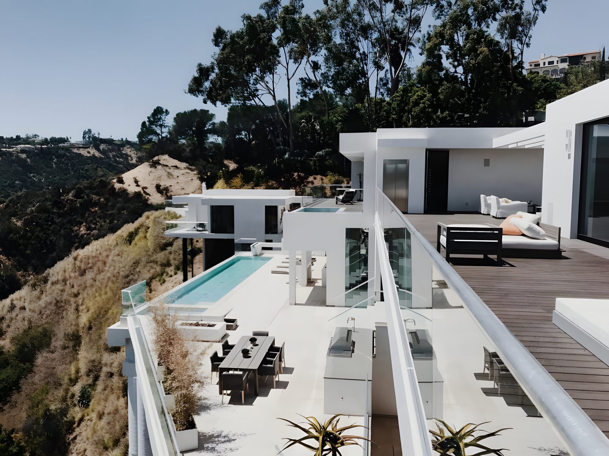 White hillside home in Bel Air with a glass balustrade, timber deck, outdoor dining terrace and infinity pool above a canyon