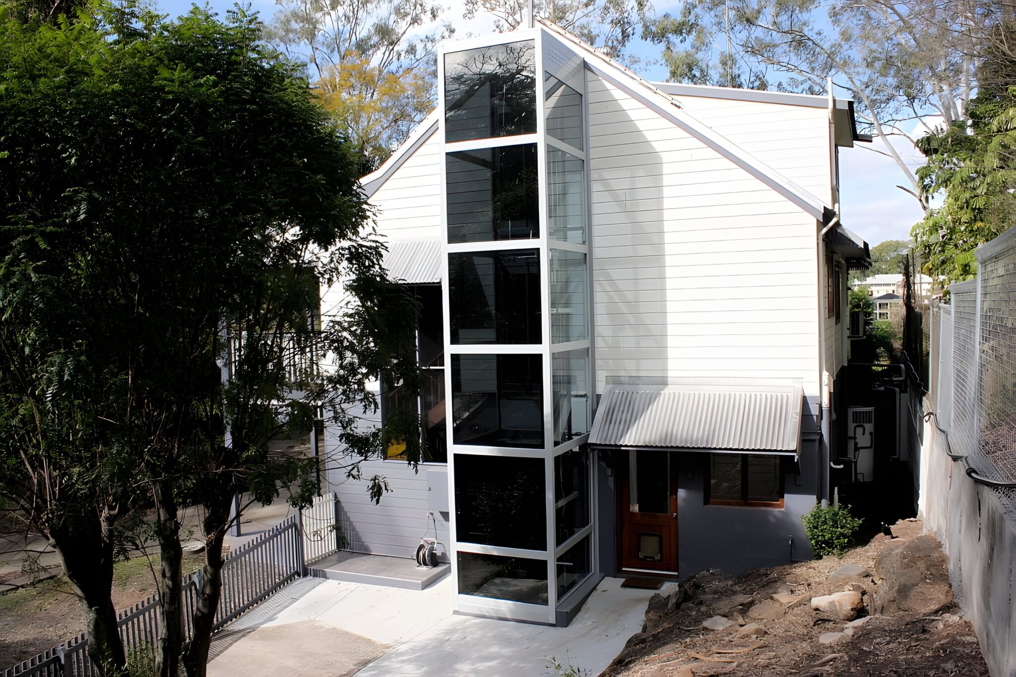 Tall glass and steel lift shaft on the front of a white and grey Queenslander-style home in Indooroopilly