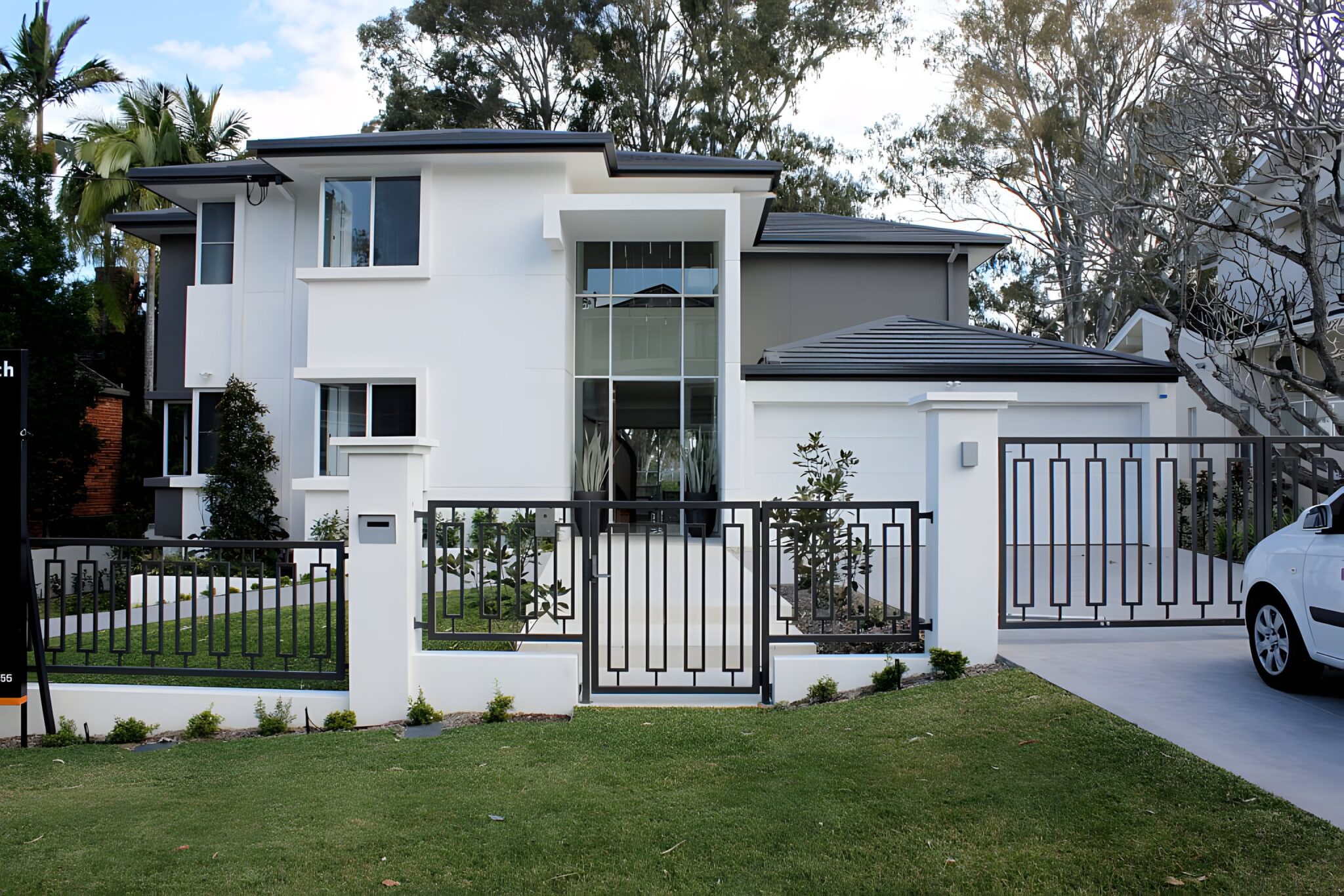 White two-storey home with a glass entry void and dark gates on a riverside street in Indooroopilly, Brisbane