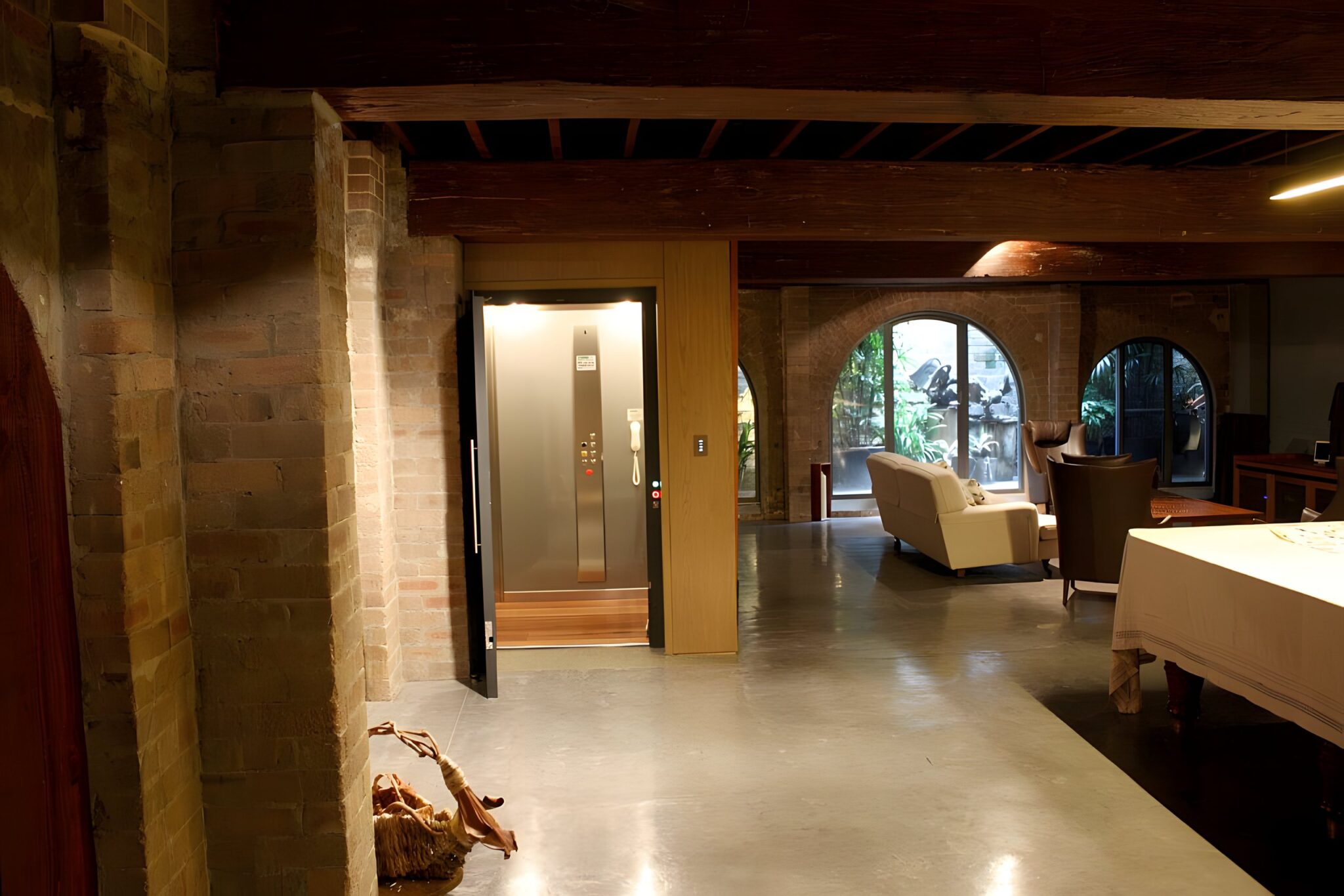 Converted warehouse living space with brick columns, polished concrete floor and the lift door in view